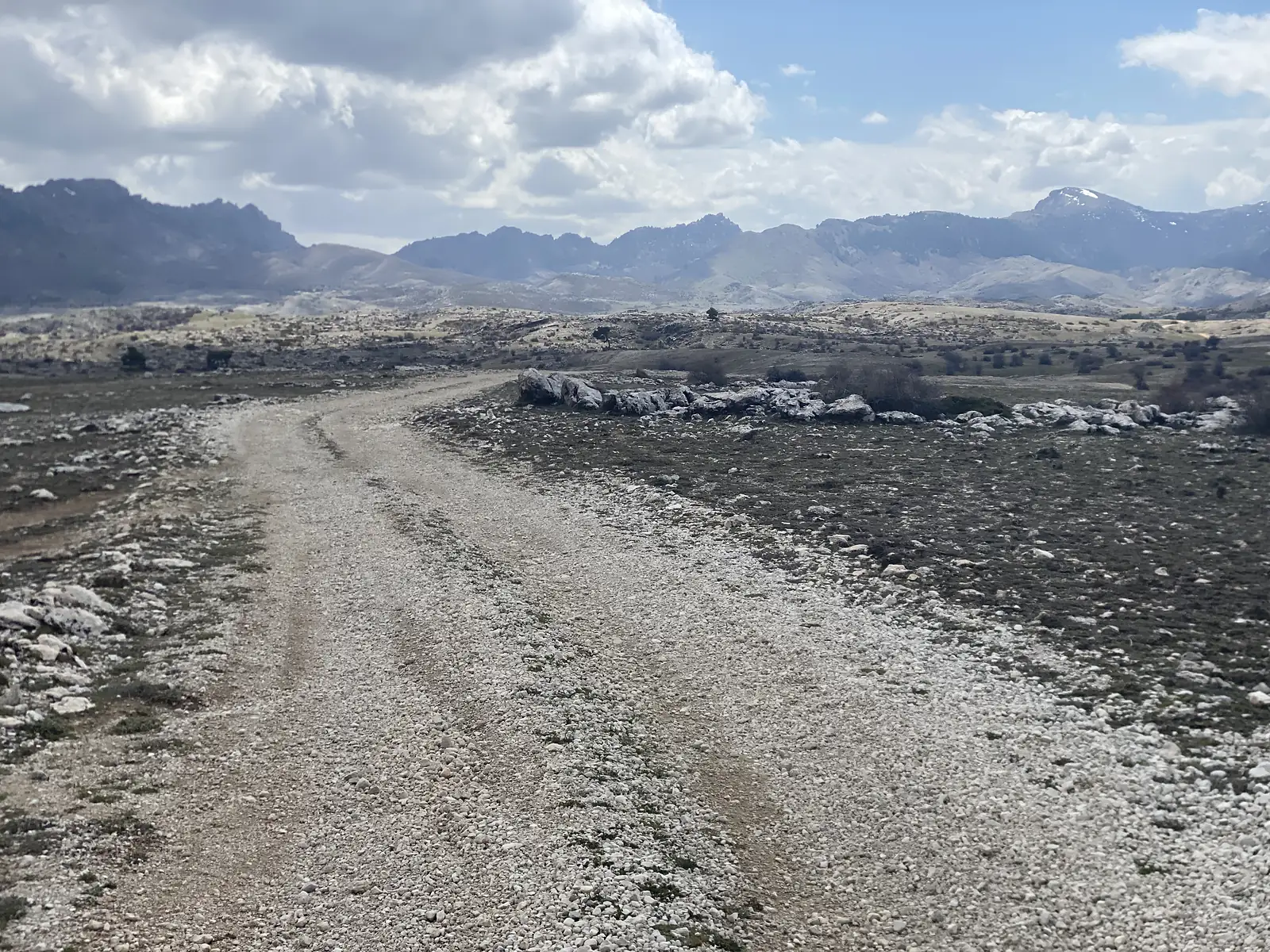 A gravel track running across a high limestone plateau towards a distant jagged range with snow on its highest peak.