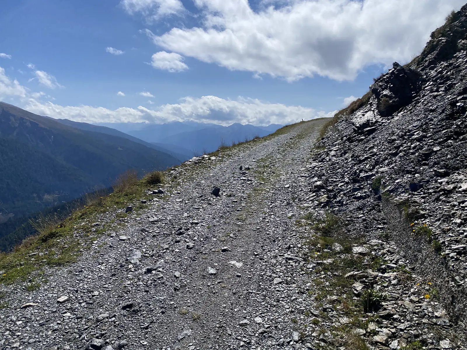 A loose, steep stony track climbs beside a shattered scree slope, with hazy blue ridges falling away below.