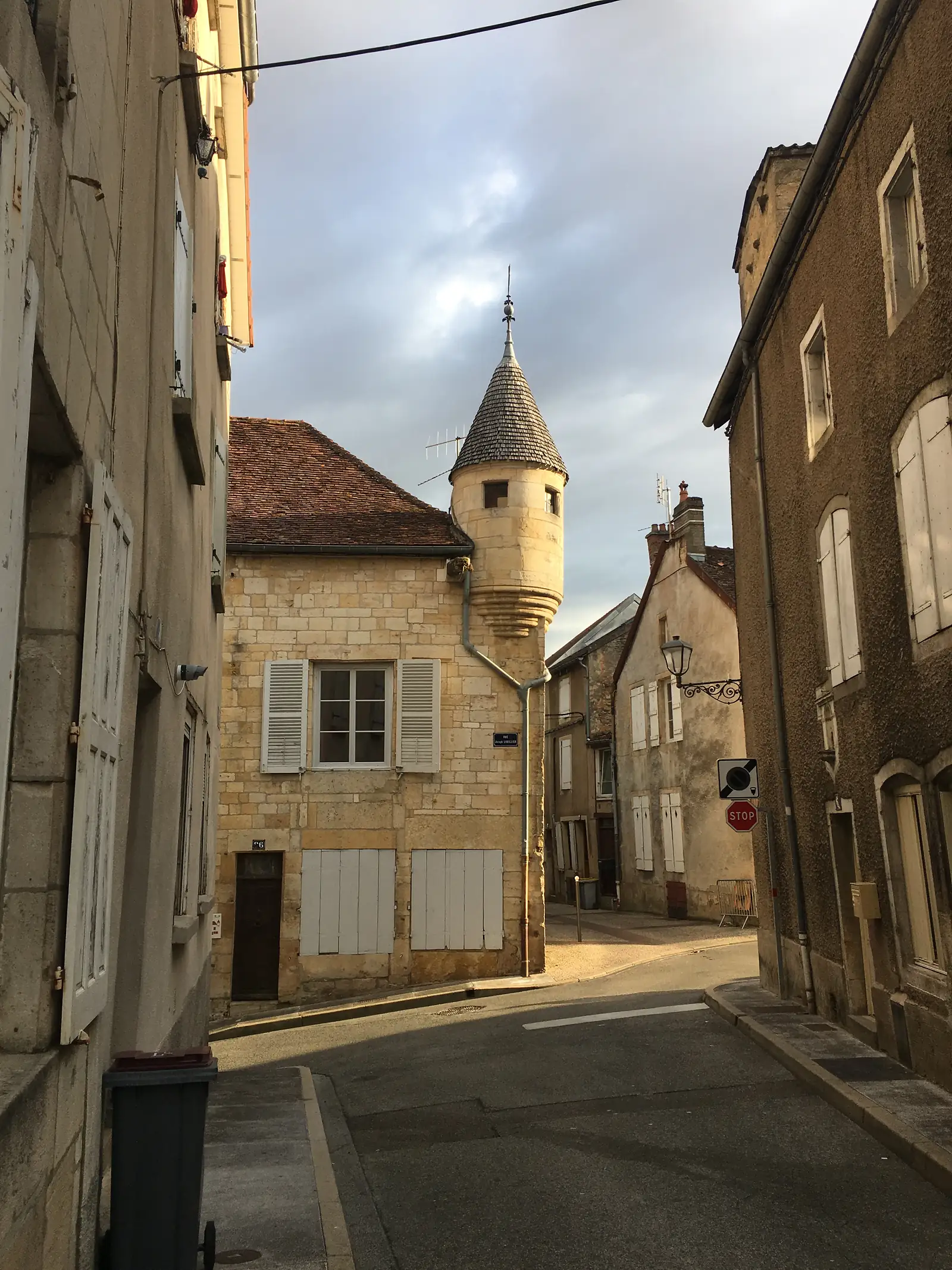 A conical stone corner turret capping a tall townhouse on a quiet Langres street, its slate roof rising above tiled neighbouring rooftops.