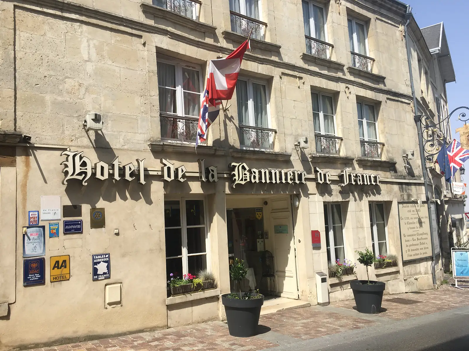 The gilded lettering of the 'Hôtel de la Bannière de France' sign spans the entrance, flanked by guide-book plaques and pots of flowers either side of the door.