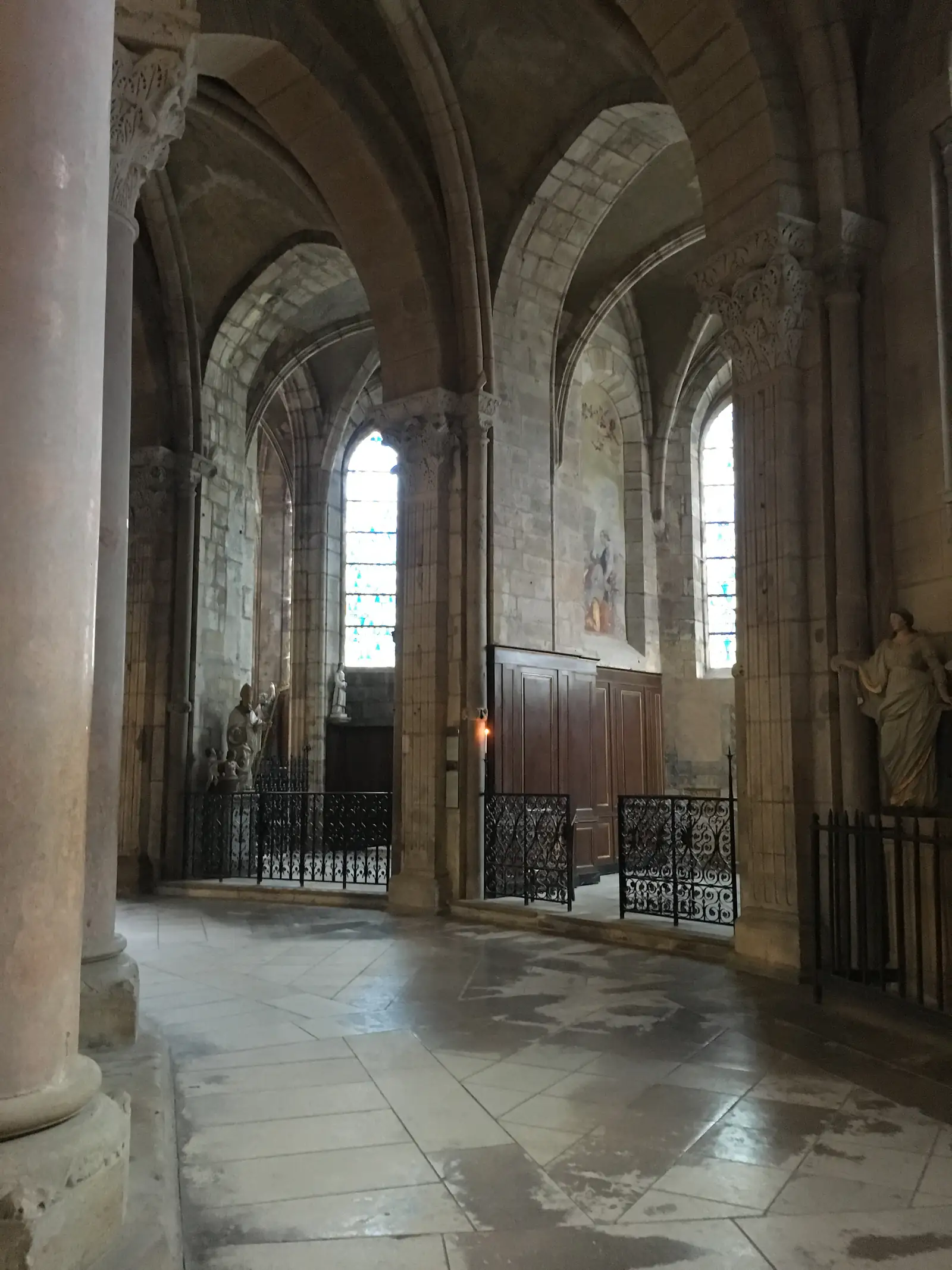 Rows of church pews facing a side chapel with stained-glass windows, a lit candle and a carved wooden door beyond an iron screen.