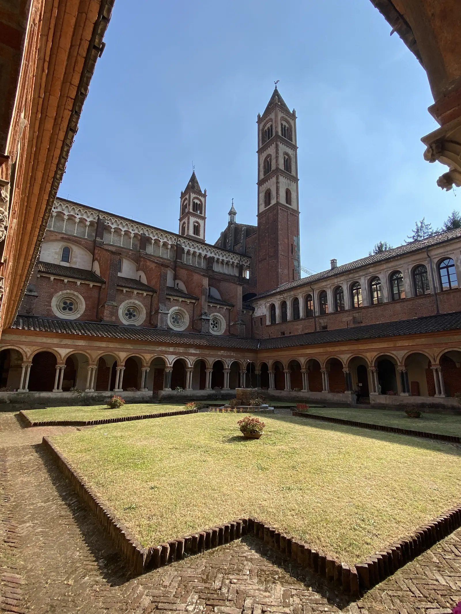 The cloister of the Basilica of Sant'Andrea, its arcaded walkway and central well garden set beneath the church's brick bell towers.