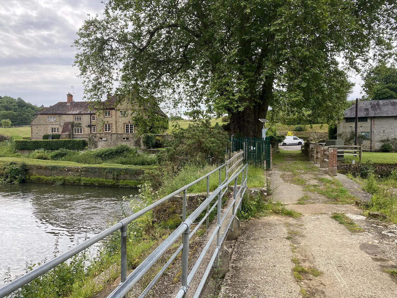 A concrete ford and railed footbridge crossing a river beside a stone farmhouse and outbuildings.