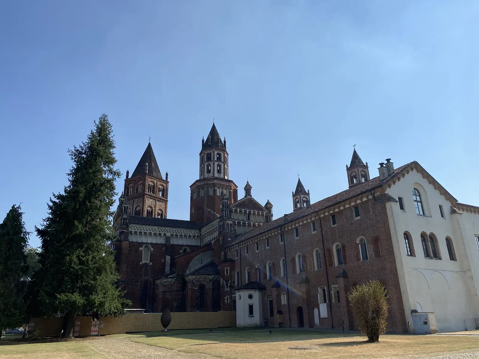 The red-brick Romanesque towers and apse of the Basilica of Sant'Andrea in Vercelli, rising above a monastic wing and a tall conifer.