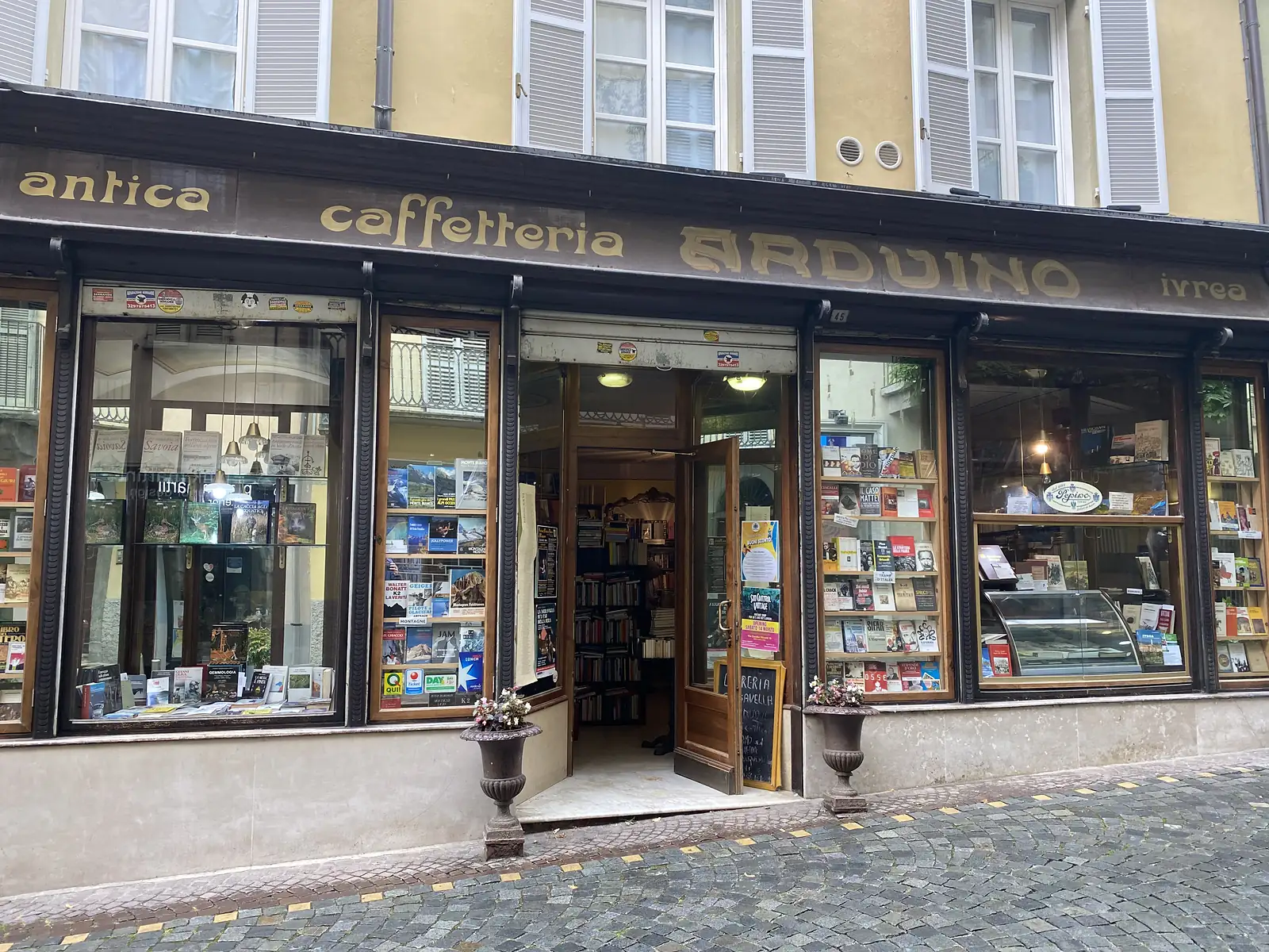 The gold-lettered shopfront of 'Antica Caffetteria Arduino' in Ivrea, its windows crammed with books, magazines and a glass-fronted pastry counter.