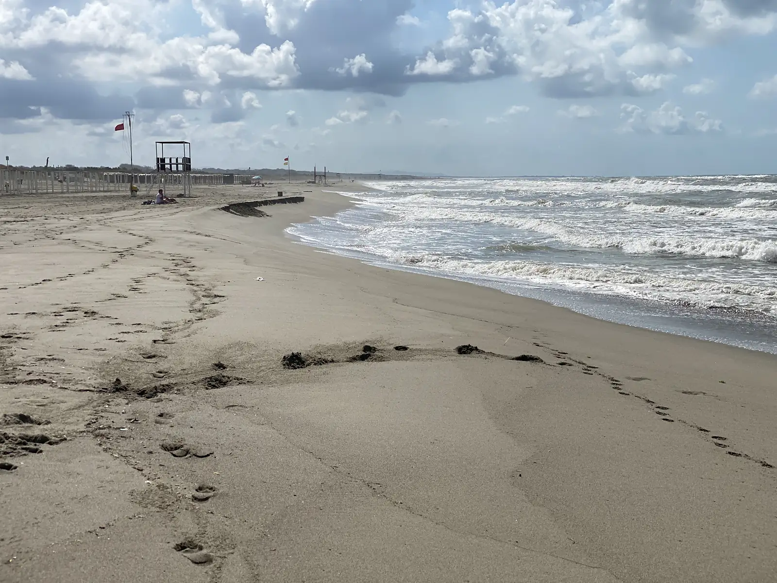 A wide sandy beach with a lifeguard tower and furled umbrellas, dog paw prints leading down towards the surf.