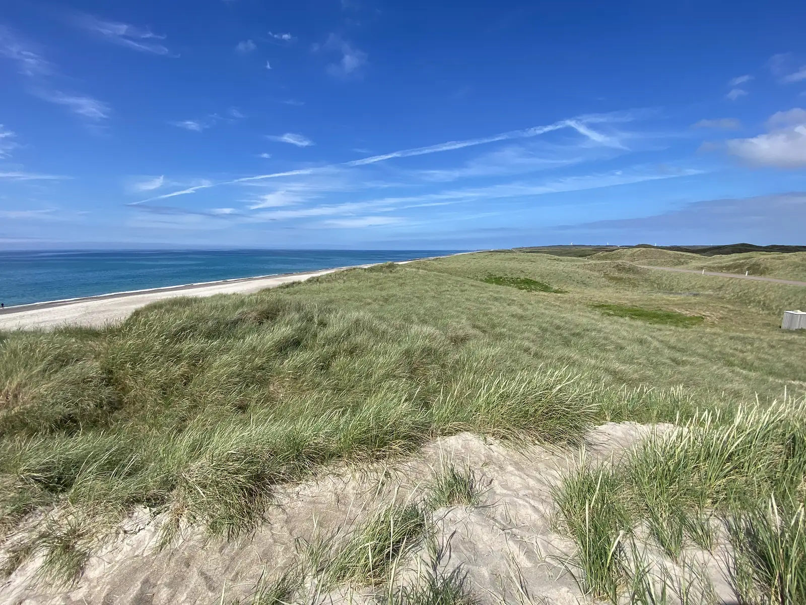 Marram-grassed dunes rolling away above a pale shingle beach and turquoise sea, with a road threading between them.