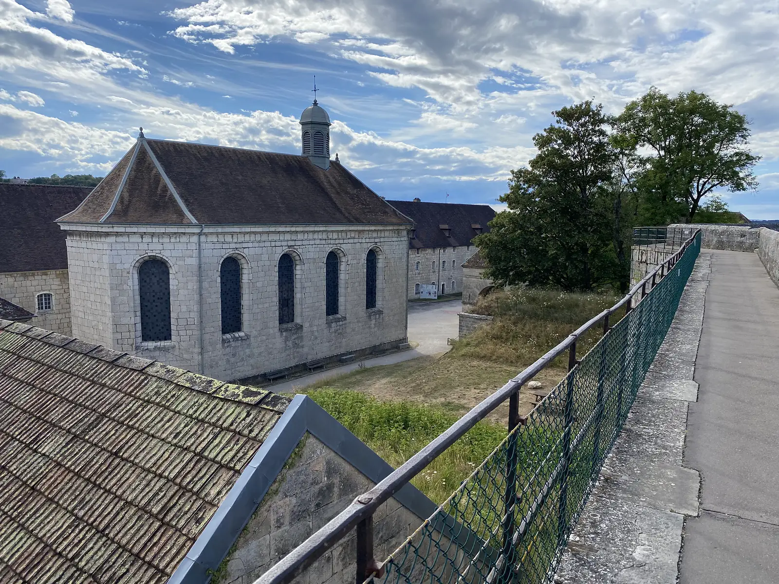A stone chapel with a tiled roof and small cupola stands among citadel buildings, seen from an adjoining rampart walkway.