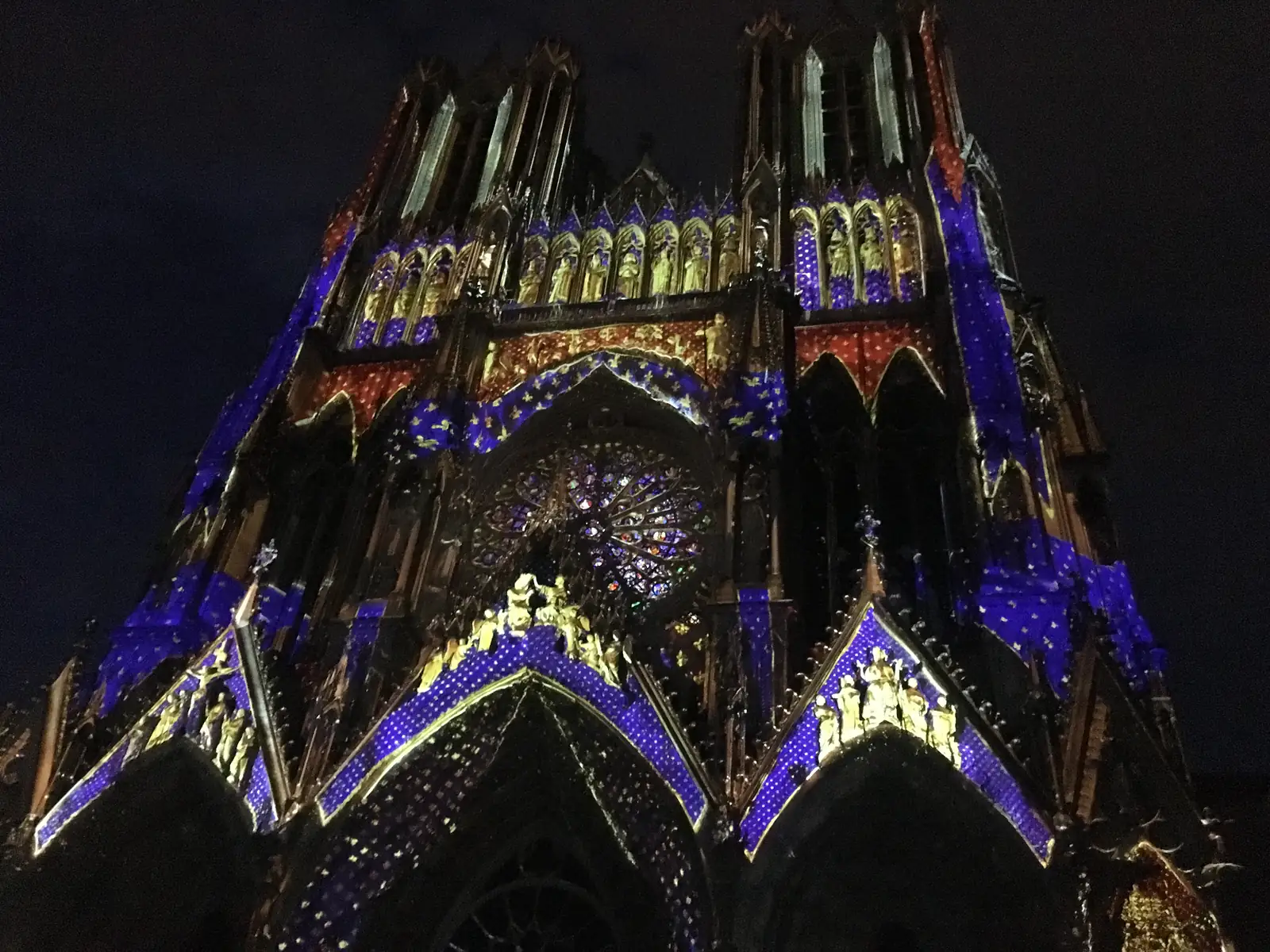 Reims cathedral's façade is lit up at night with a projected starry blue and gold design covering its gables, statues and rose window.