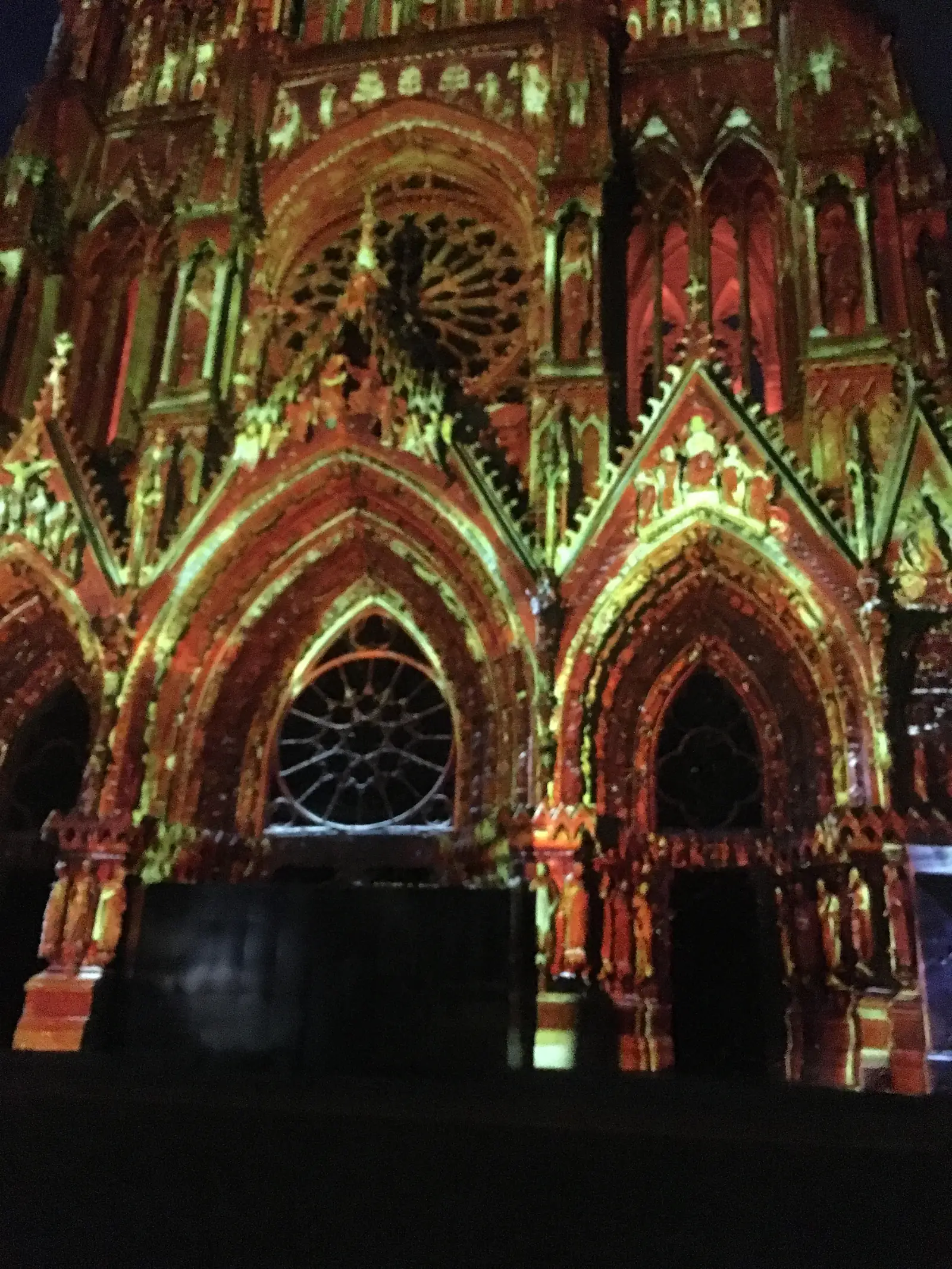 A blurred night-time light projection bathes the cathedral's rose window and gables in deep red and gold patterns during an illuminated son-et-lumière show.
