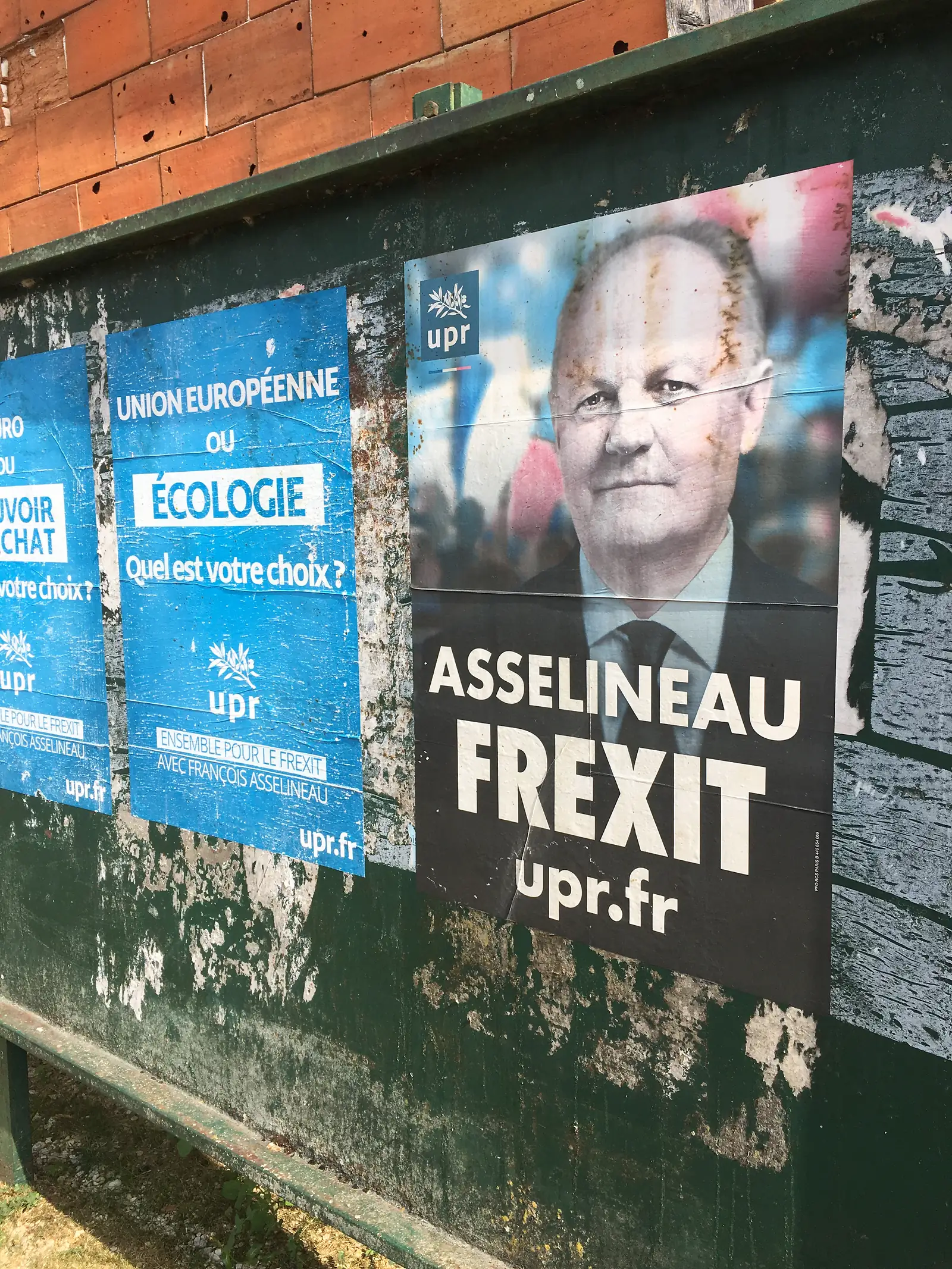 A weathered election poster for Asselineau's FREXIT campaign is pasted over older UPR posters on a noticeboard.