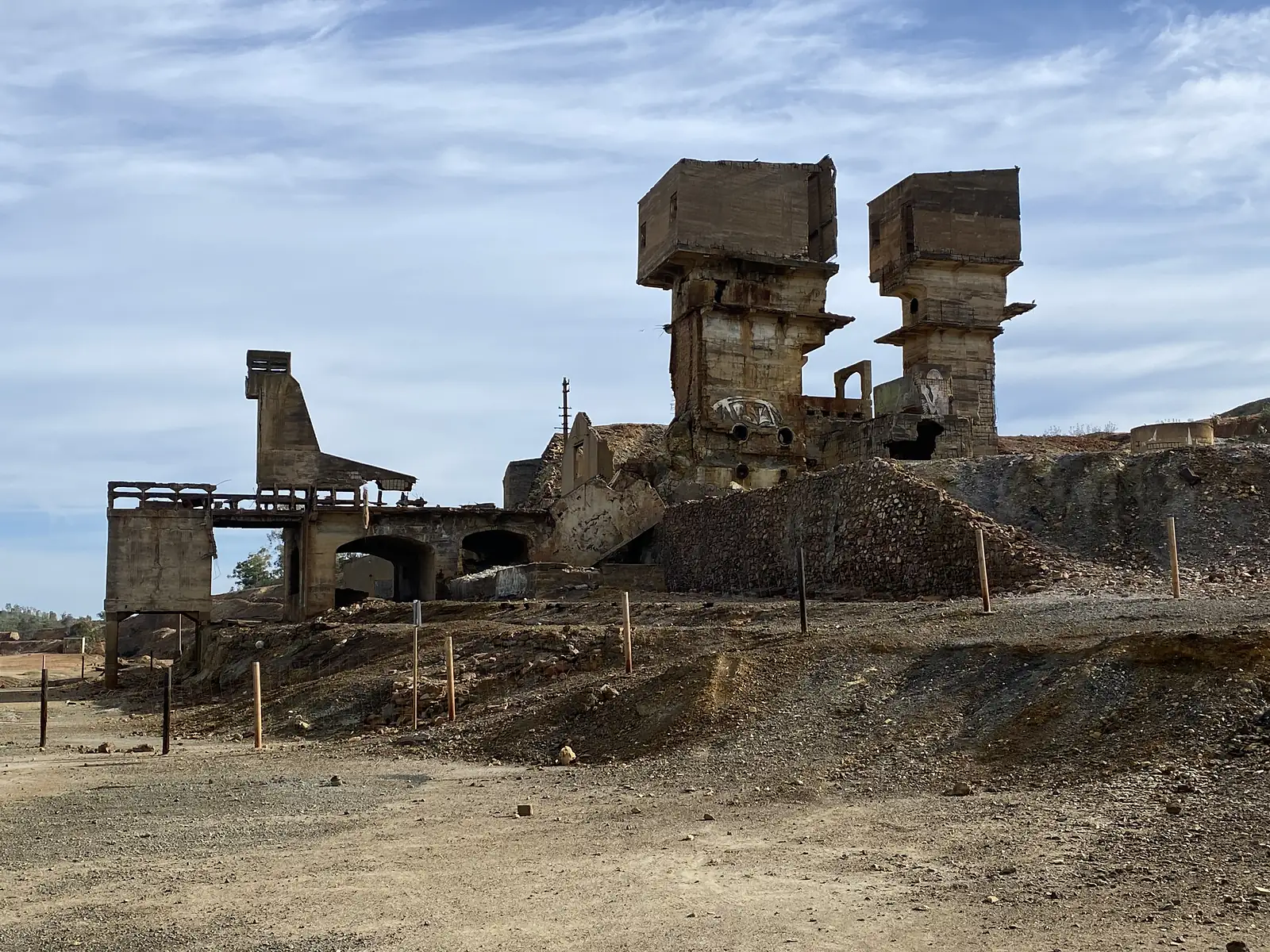 The gutted concrete towers and arches of an abandoned mine works standing above bare orange spoil heaps.