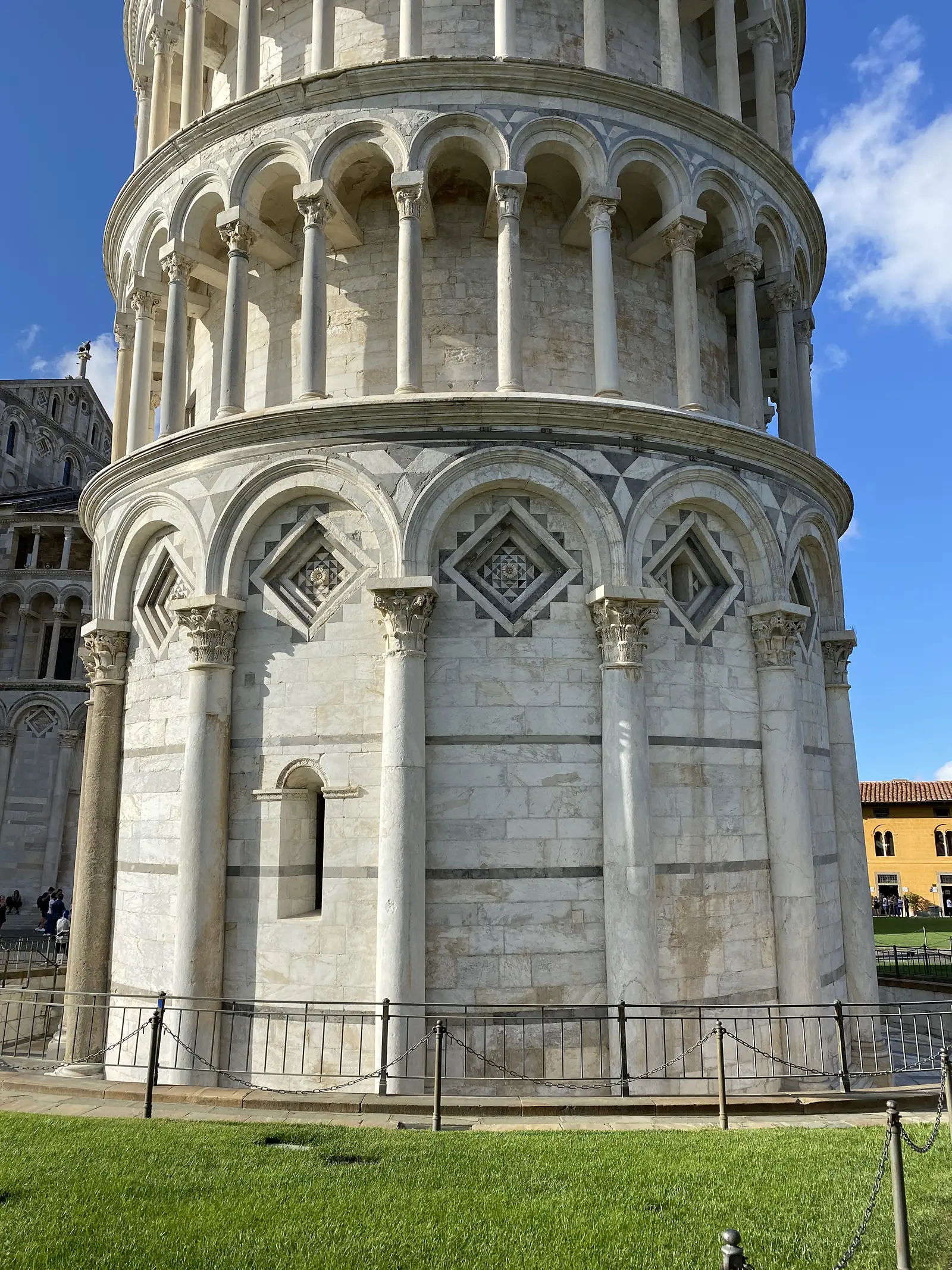 A close view of the Leaning Tower's carved marble arcading, its columns and diamond-patterned inlay tilting noticeably against the sky.