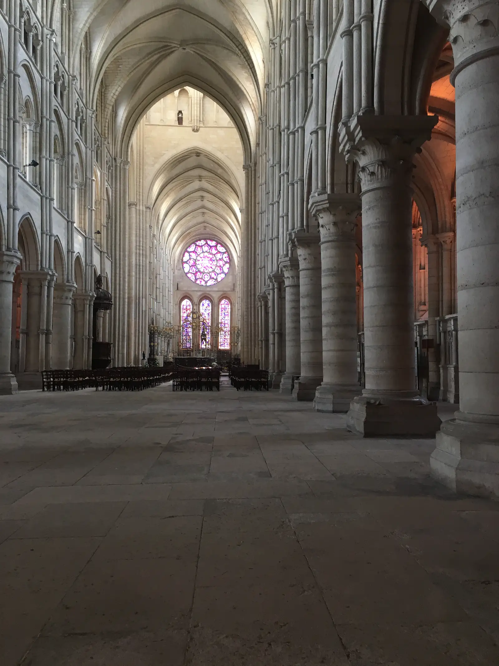 Inside the cathedral, ranks of stone columns lead down the nave towards a glowing stained-glass rose window at the far end.