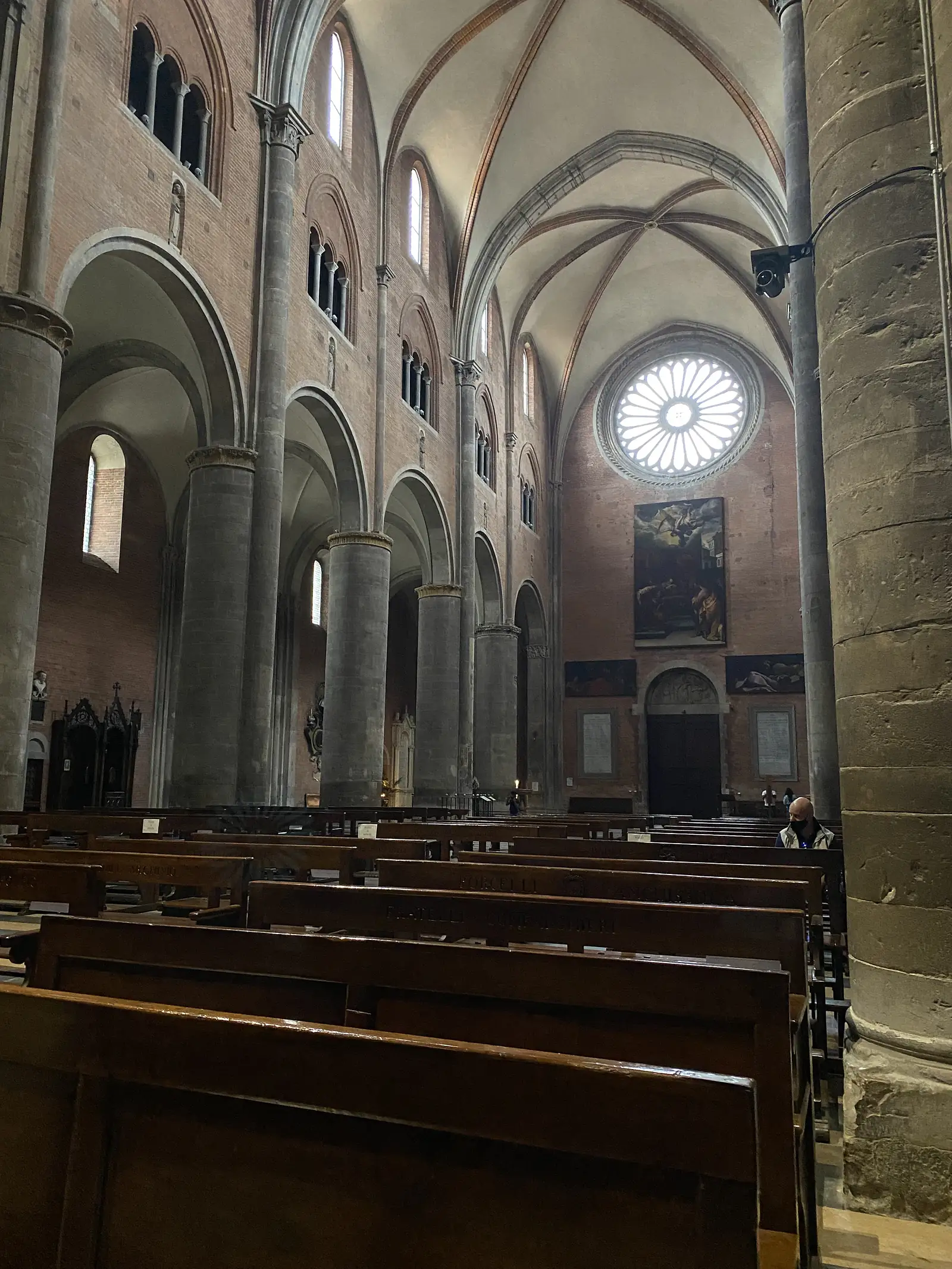 The vaulted nave of a Romanesque church, its striped arches and columns leading past painted panels towards a rose window.