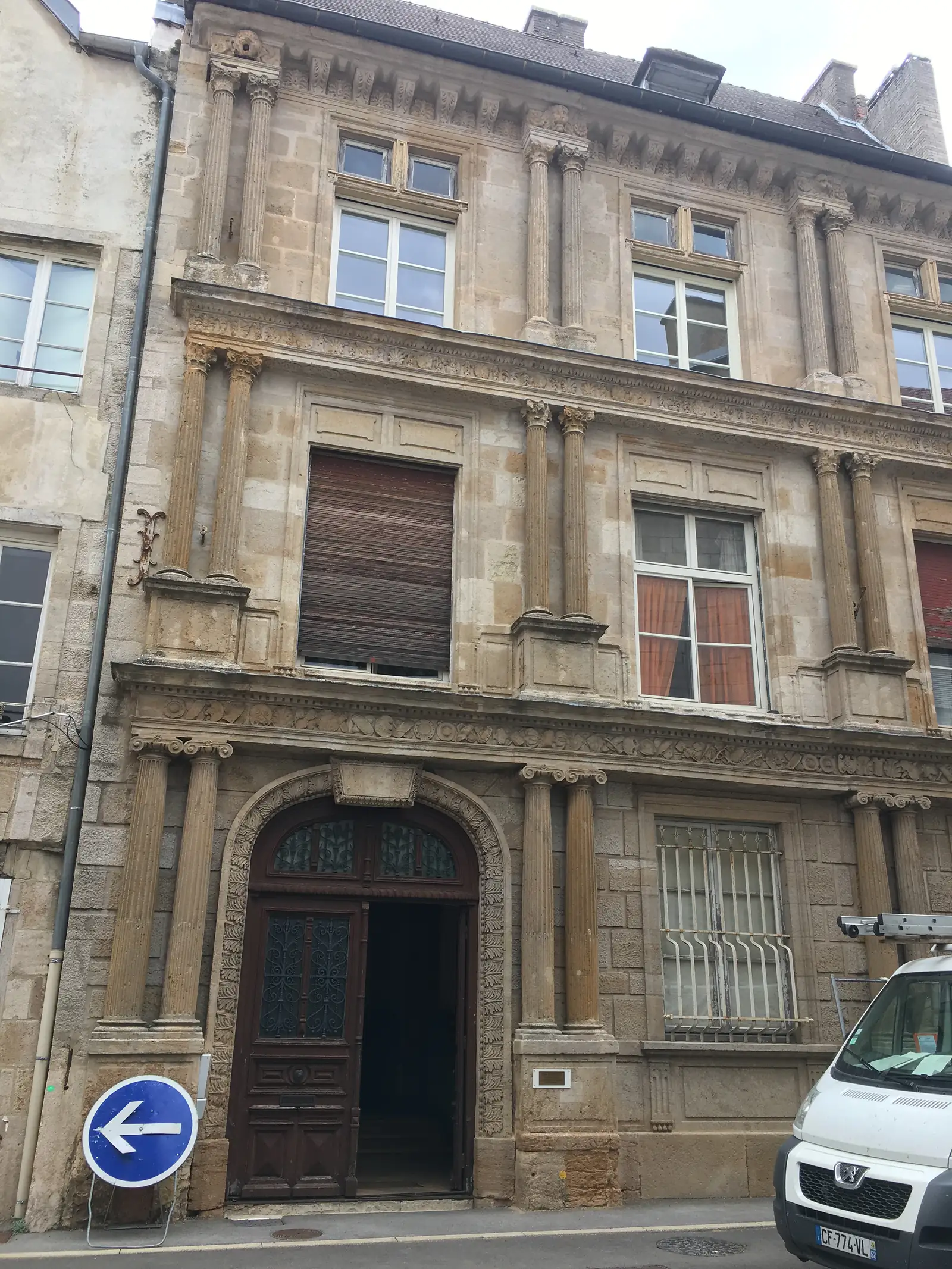 The carved stone facade of a townhouse with pilastered window surrounds and an arched doorway with wrought-iron grille, a delivery van parked outside.