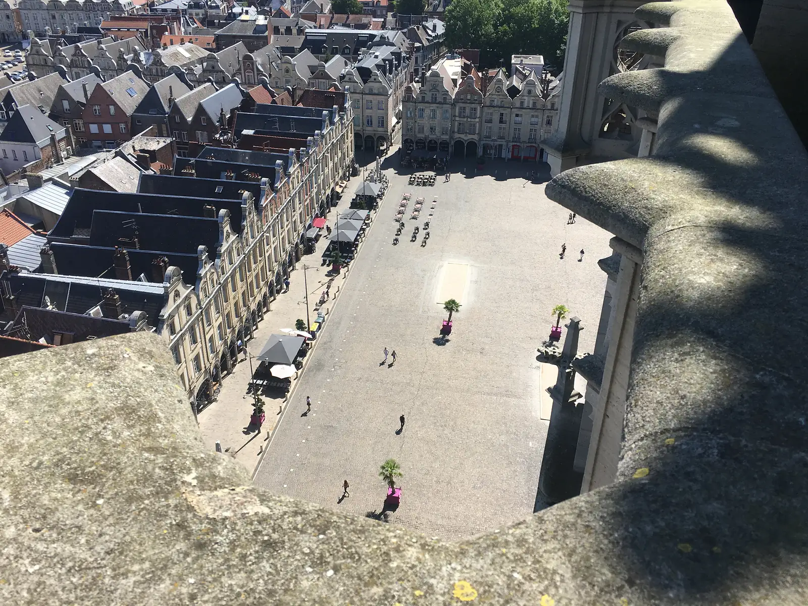 A wide view over Arras's rooftops from the belfry, gabled townhouses in the foreground giving way to tower blocks and open farmland on the horizon.