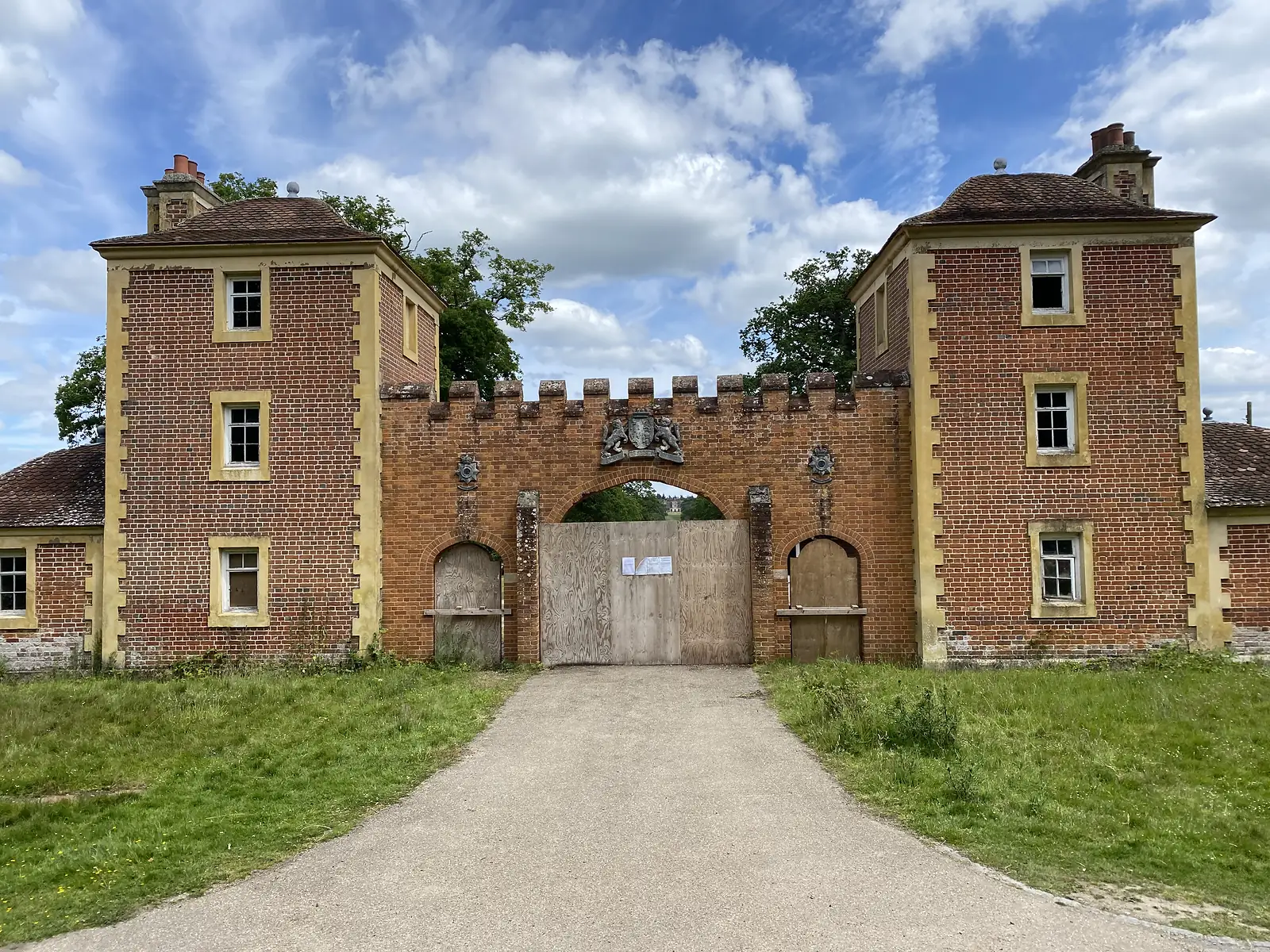 A red-brick Tudor-style gatehouse with a battlemented centre, twin towers and a coat of arms above a boarded-up arch.