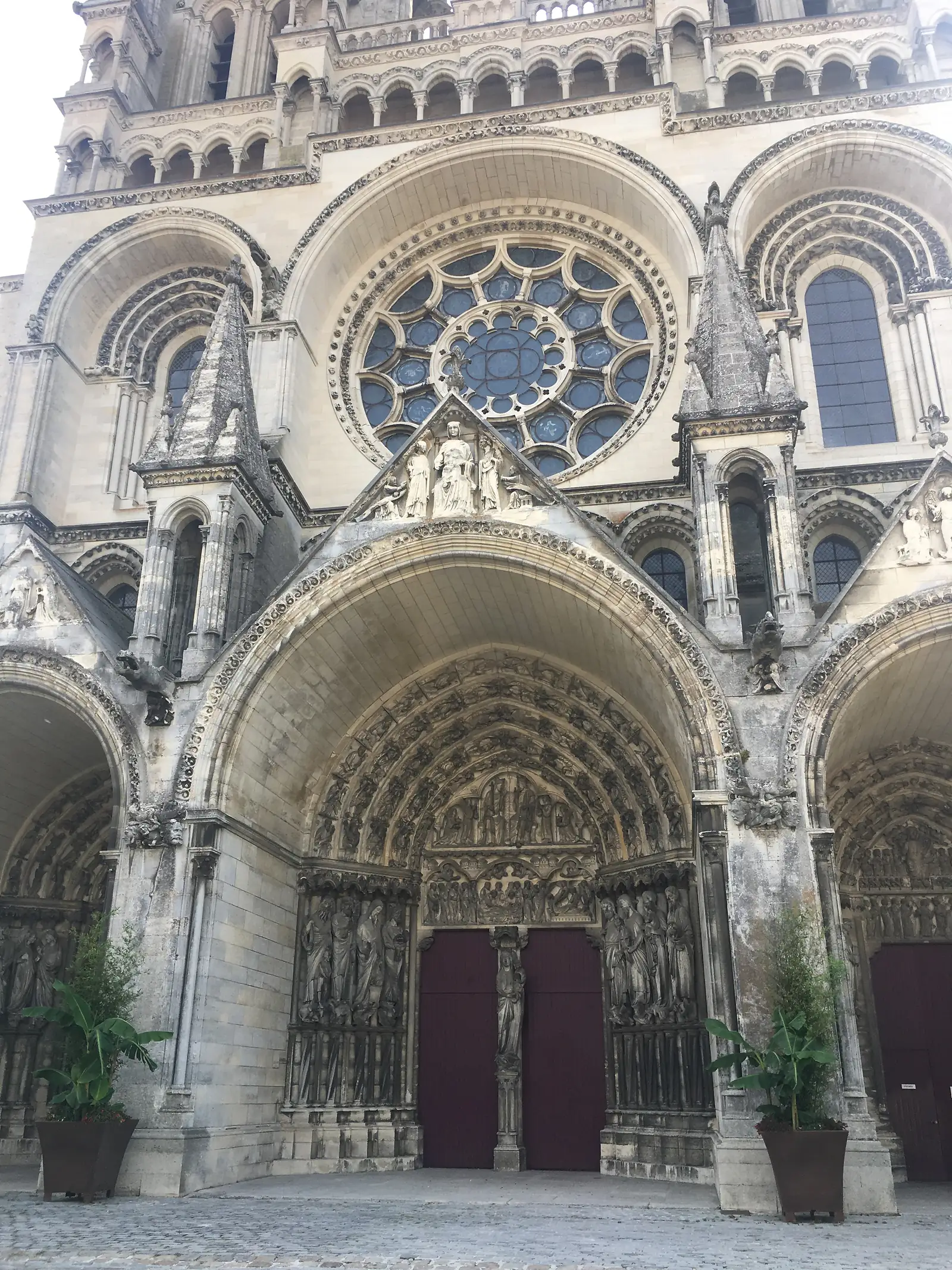 A cathedral's stone rose window with blue stained glass sits above a deeply carved arched portal lined with statues of saints.
