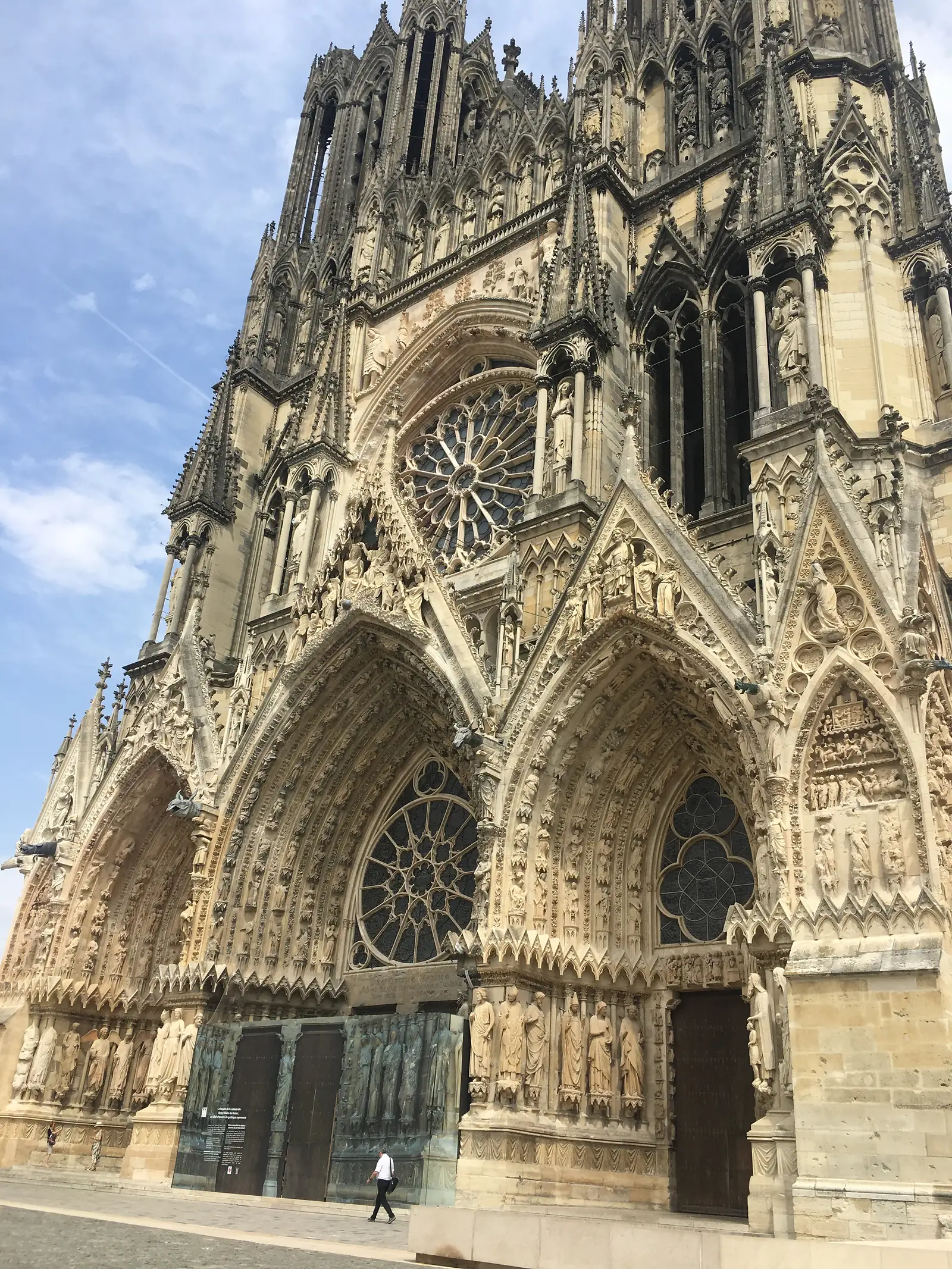 The twin towers and west facade of Reims Cathedral rising above its sculpted portals and rose window, seen from the square below.
