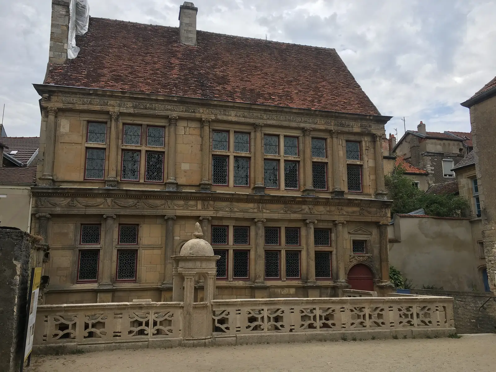 A grand Renaissance stone townhouse in Langres with two storeys of mullioned windows framed by pilasters, an ornate balustraded terrace in front and a steep tiled roof.