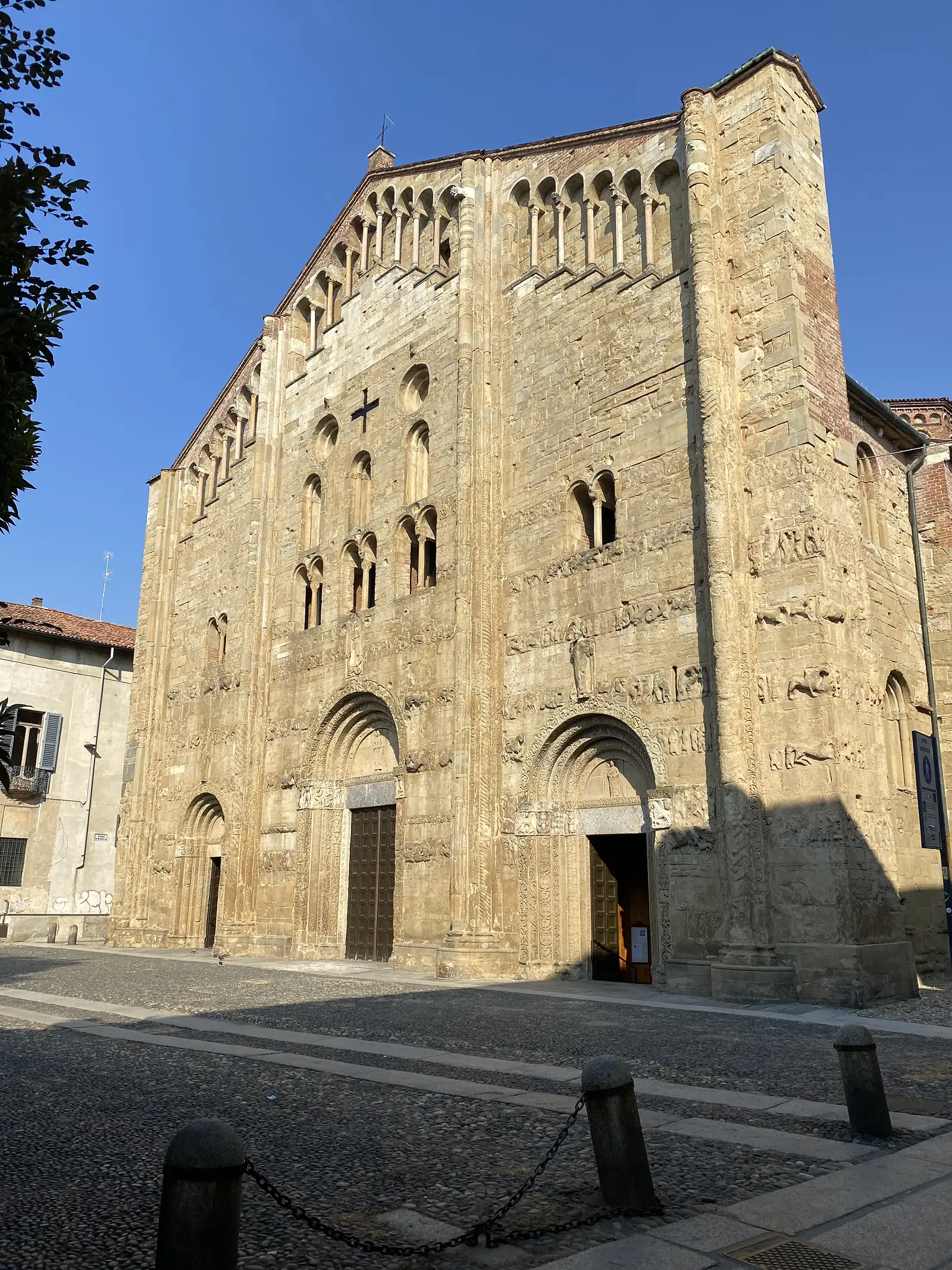 The ornately carved sandstone façade of a Romanesque church rises above a cobbled square, its rounded arches and blind arcading catching the evening light.