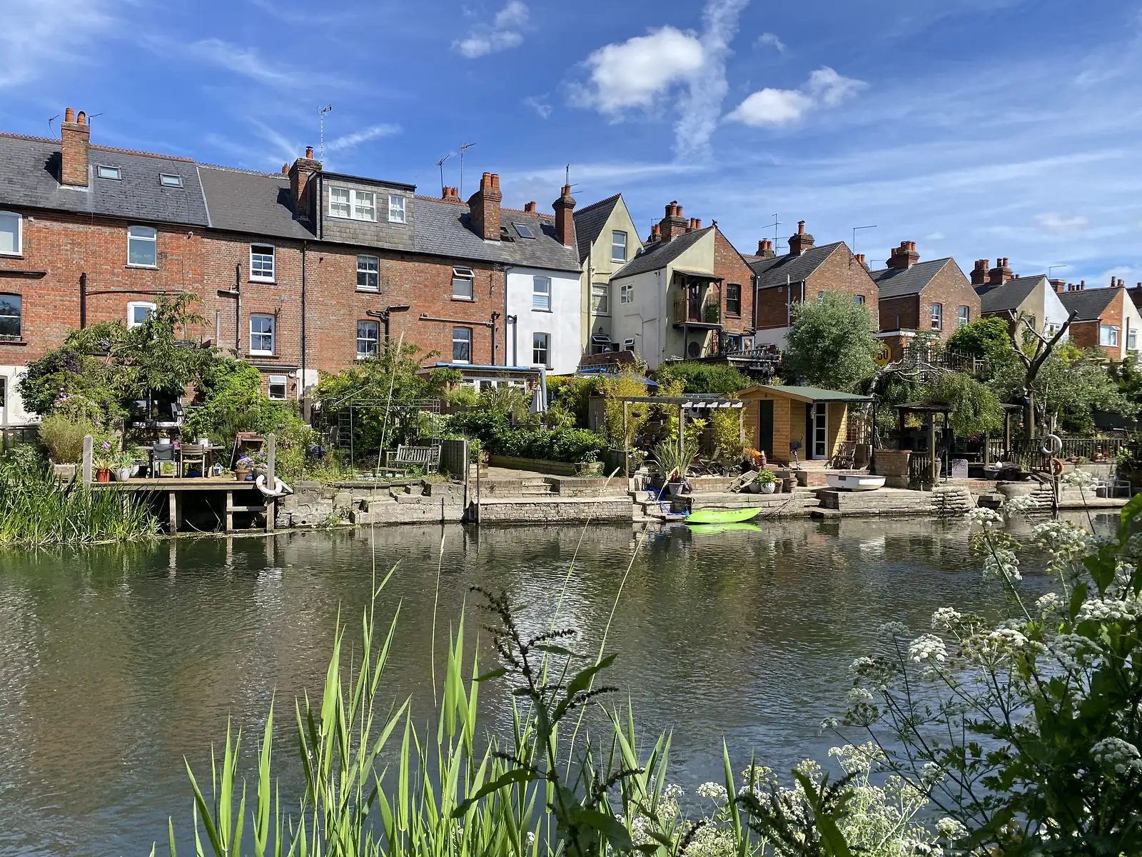 Victorian brick terraced houses with long back gardens running down to a river, a green kayak and a small boat at the water's edge.