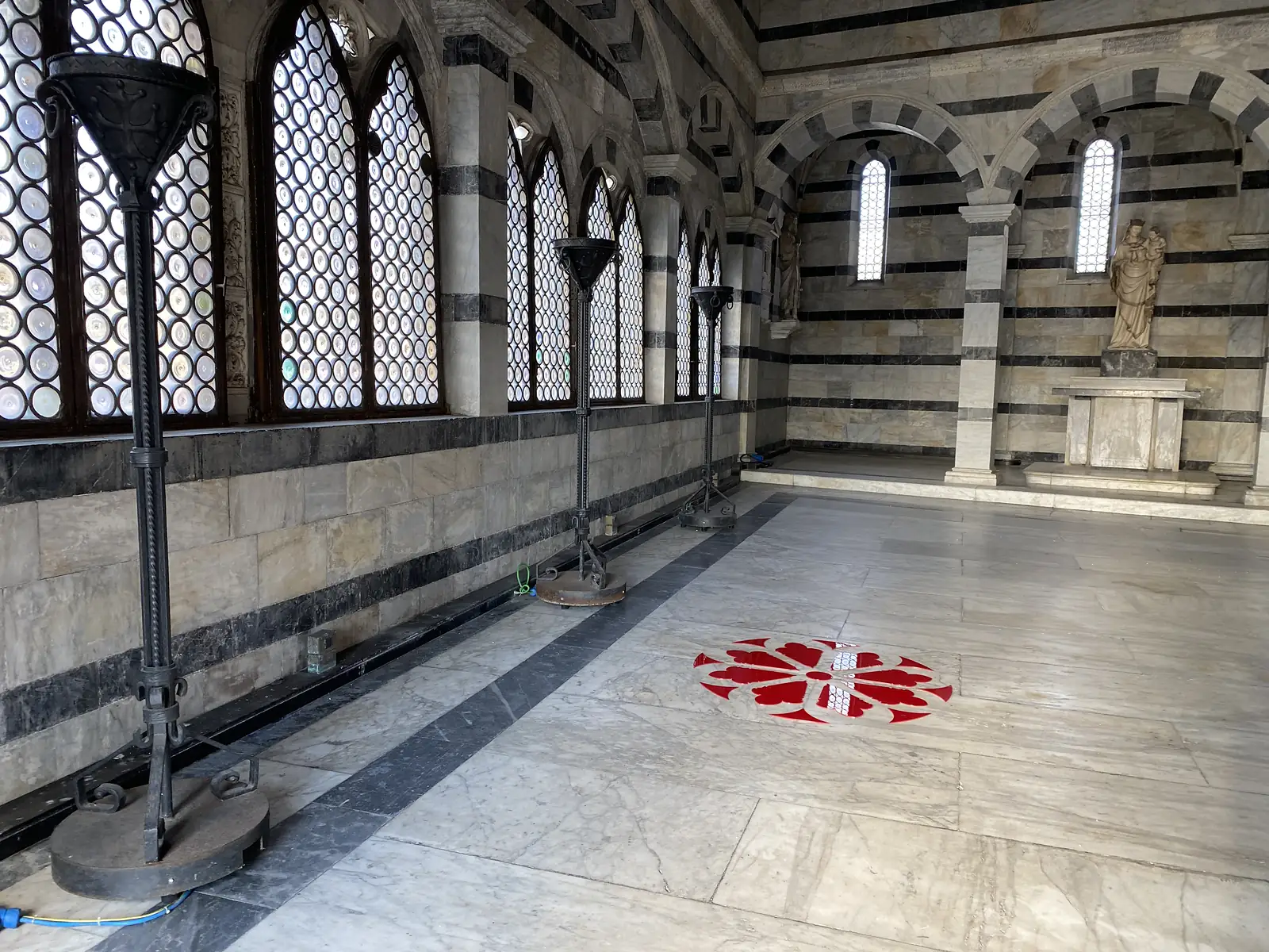 Inside a round marble chapel, stained-glass windows line one wall and a statue of the Madonna and Child stands by the altar, with a red-and-white heraldic emblem set into the floor.
