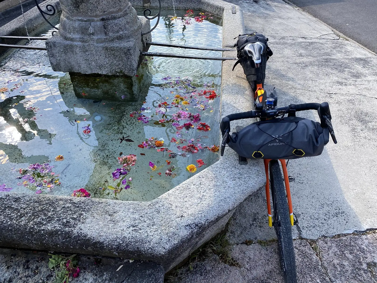 A bike leaning by a fountain with flowers in it.