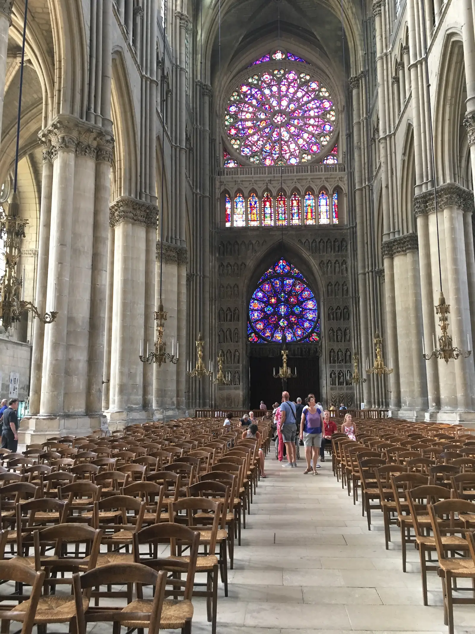 Close-up of the richly carved west front of Reims Cathedral, tiers of gothic statuary surrounding a rose window and a smaller trefoil light above the portal.