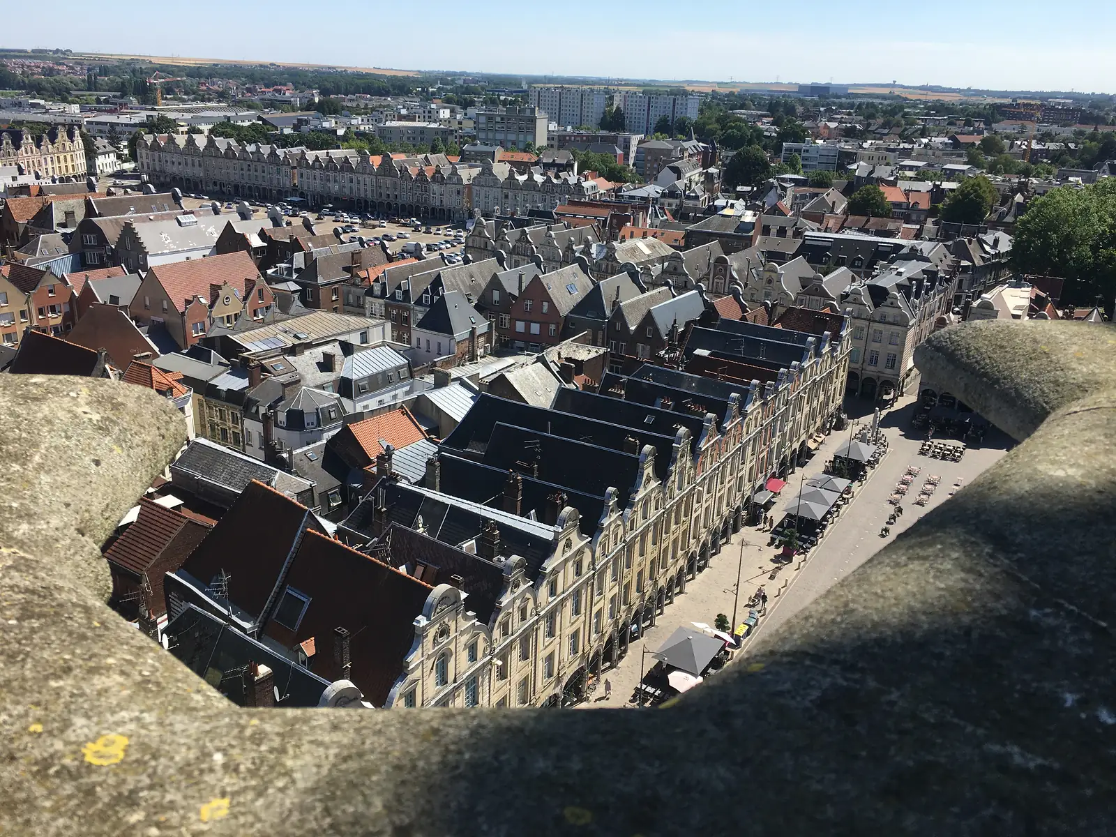 Arras's rooftops and a long classical barracks building seen from the belfry, with twin tower blocks and open countryside in the distance.