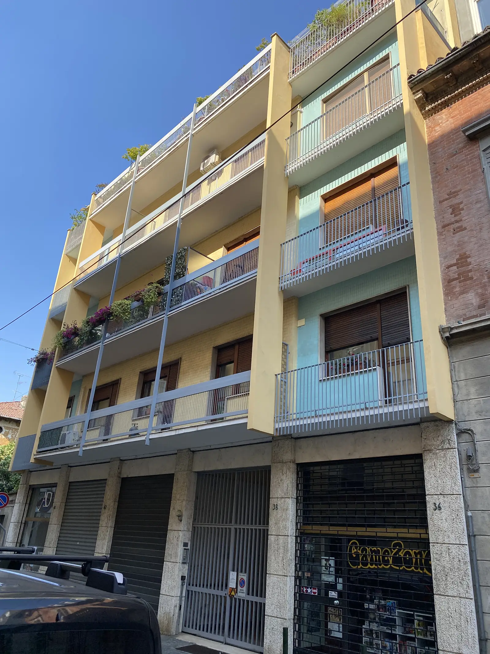 A tall stuccoed apartment block with balconies and awnings on a Vercelli street, a comic-shop sign visible on the building opposite.
