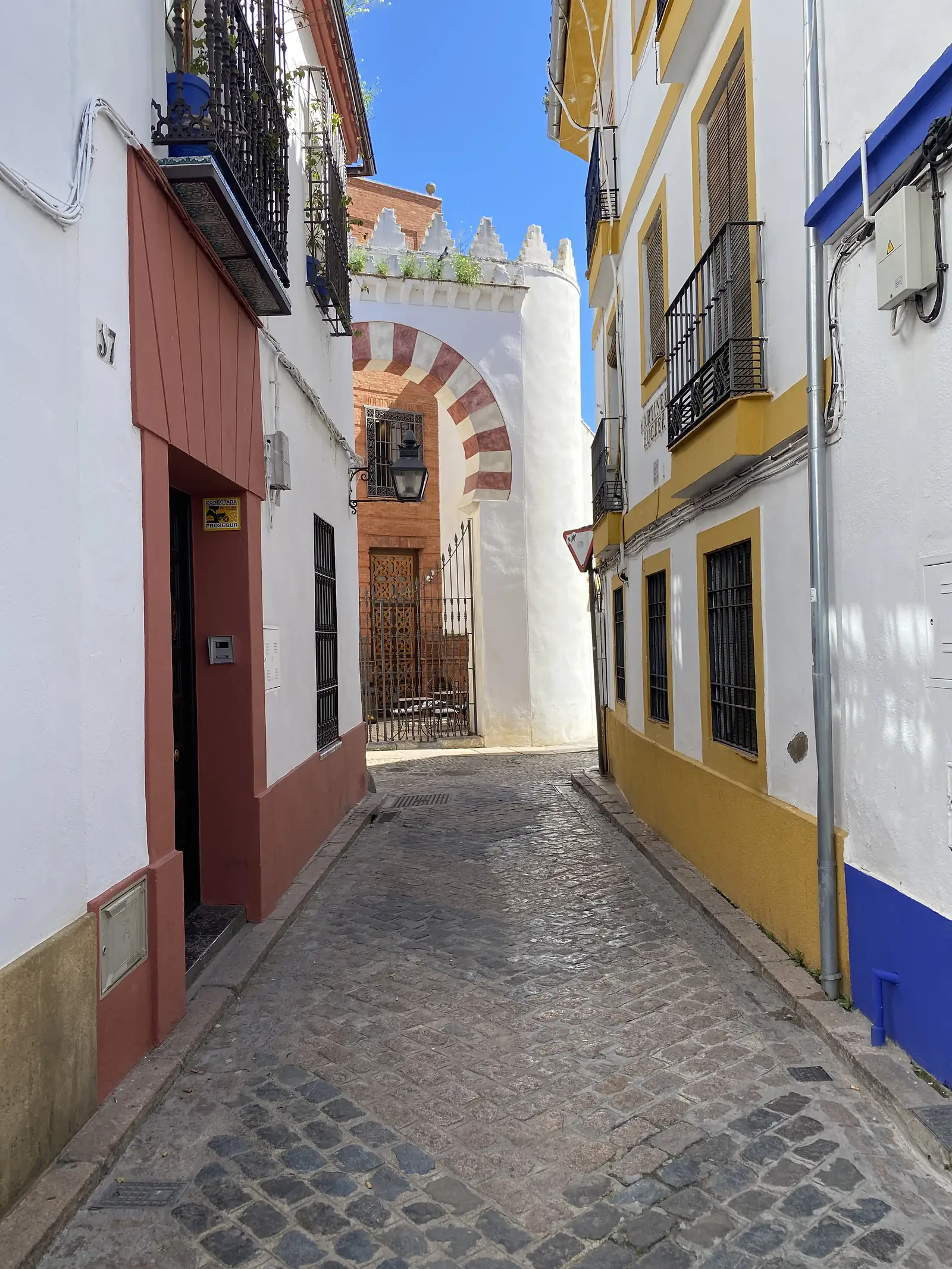 A narrow cobbled lane between white and ochre houses leading to a red-and-white striped horseshoe archway.