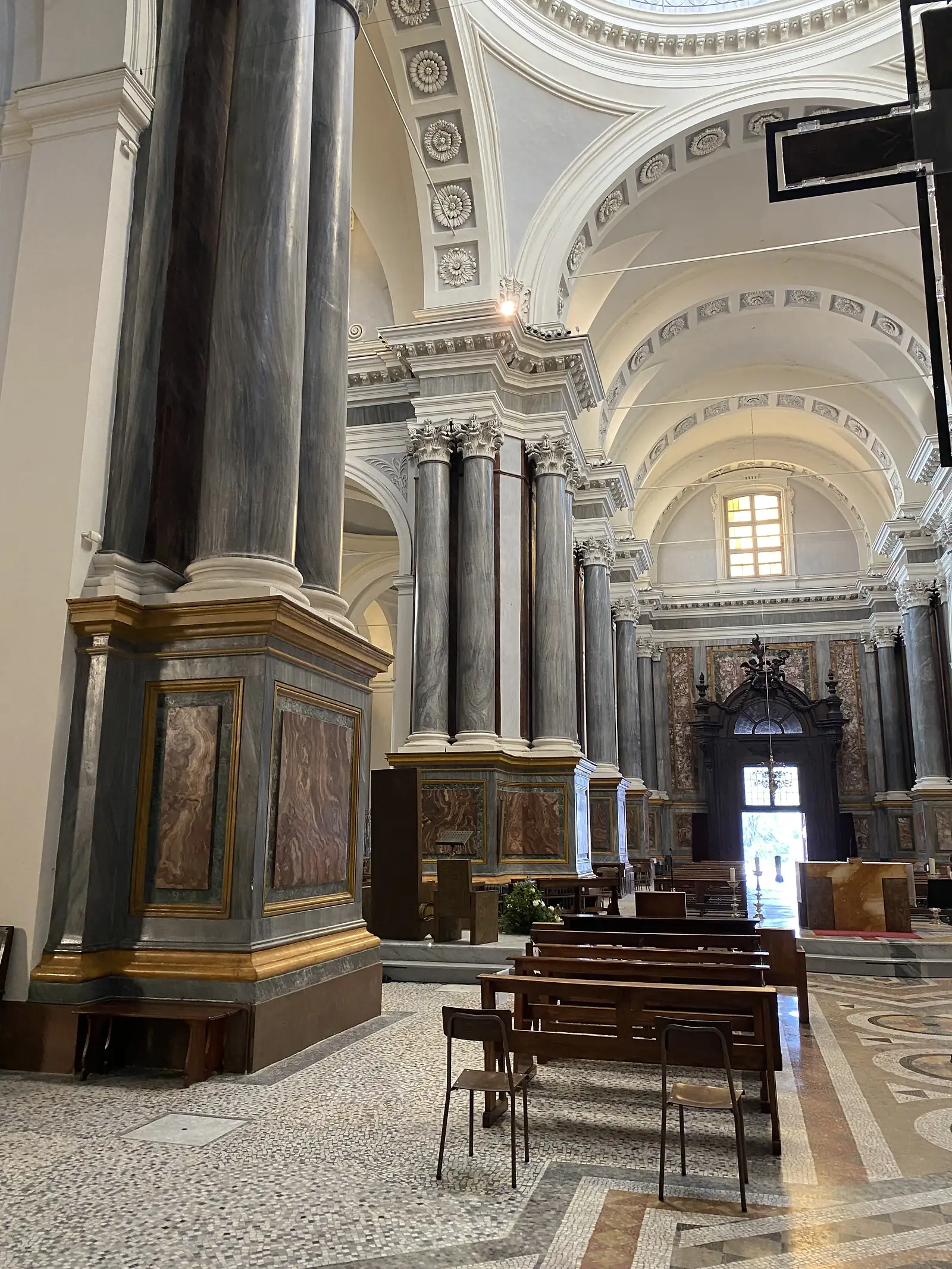 A row of grey marble columns lines the nave, leading past a carved wooden pulpit towards a bright window at the far end of the church.