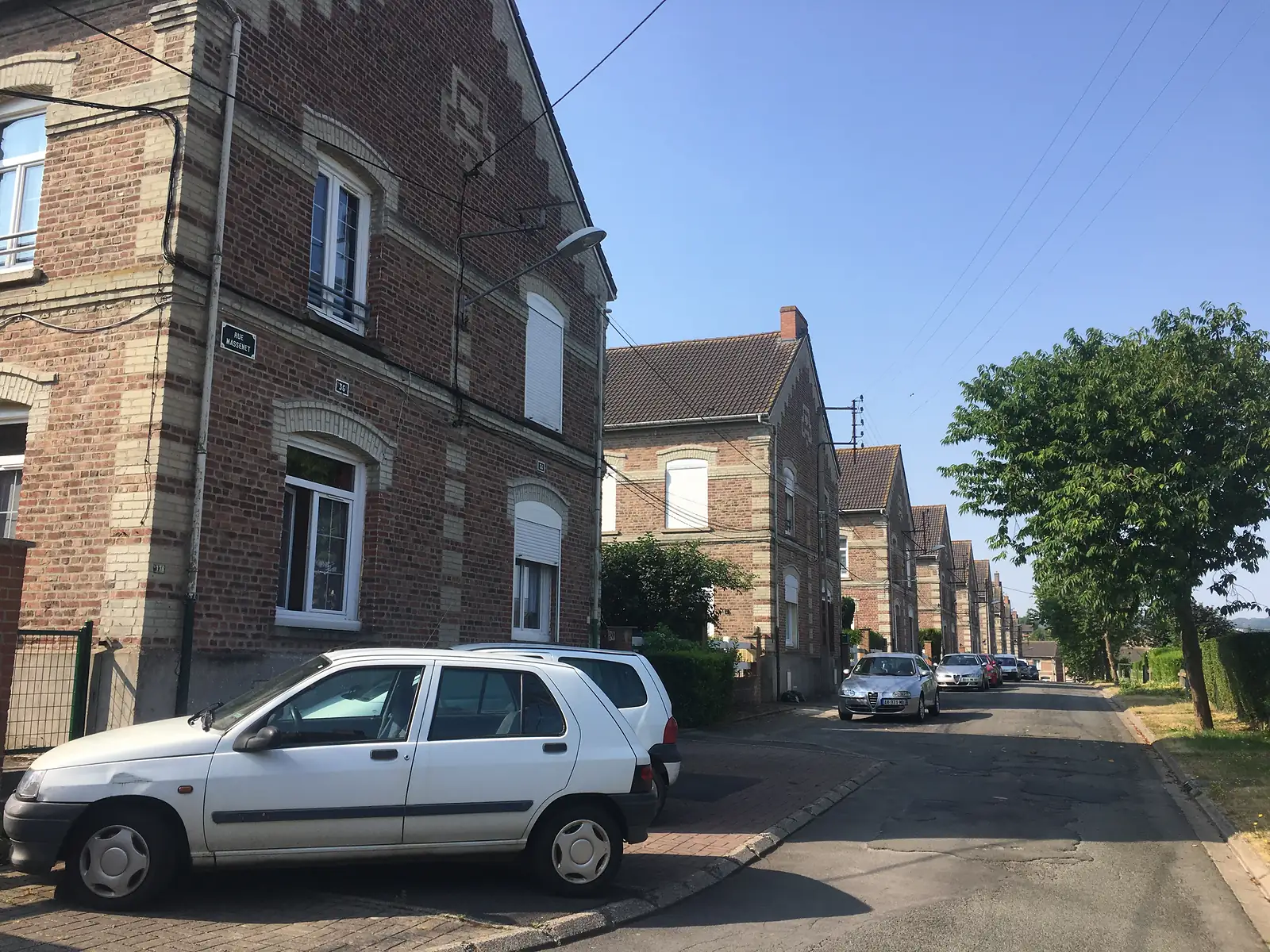 A terraced brick street named Rue Massenet in a former mining town, with cars parked along the kerb beneath a row of gabled houses.