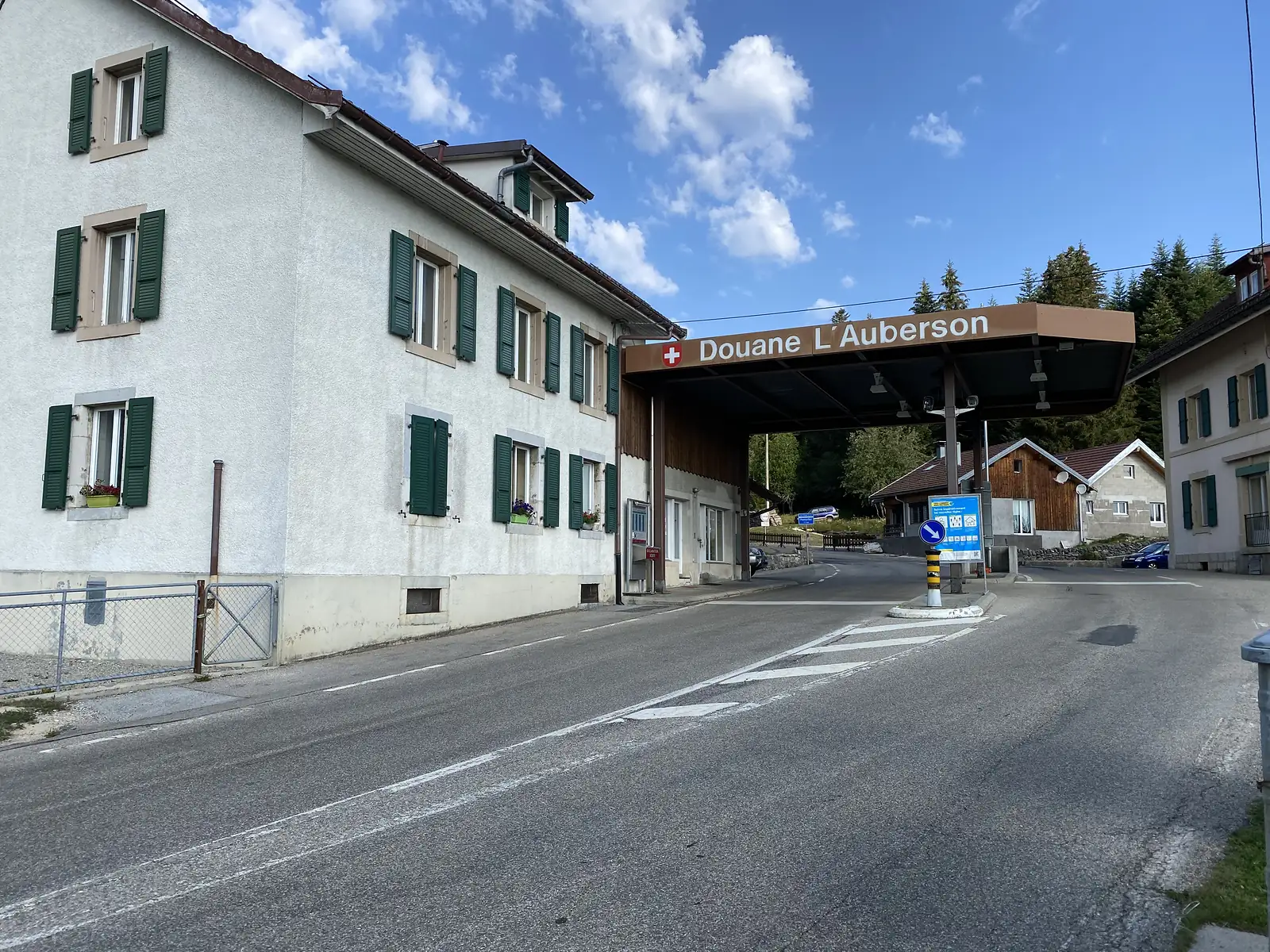 A grand shuttered building beside the brown canopy of the 'Douane L'Auberson' post, marking the French-Swiss border crossing.