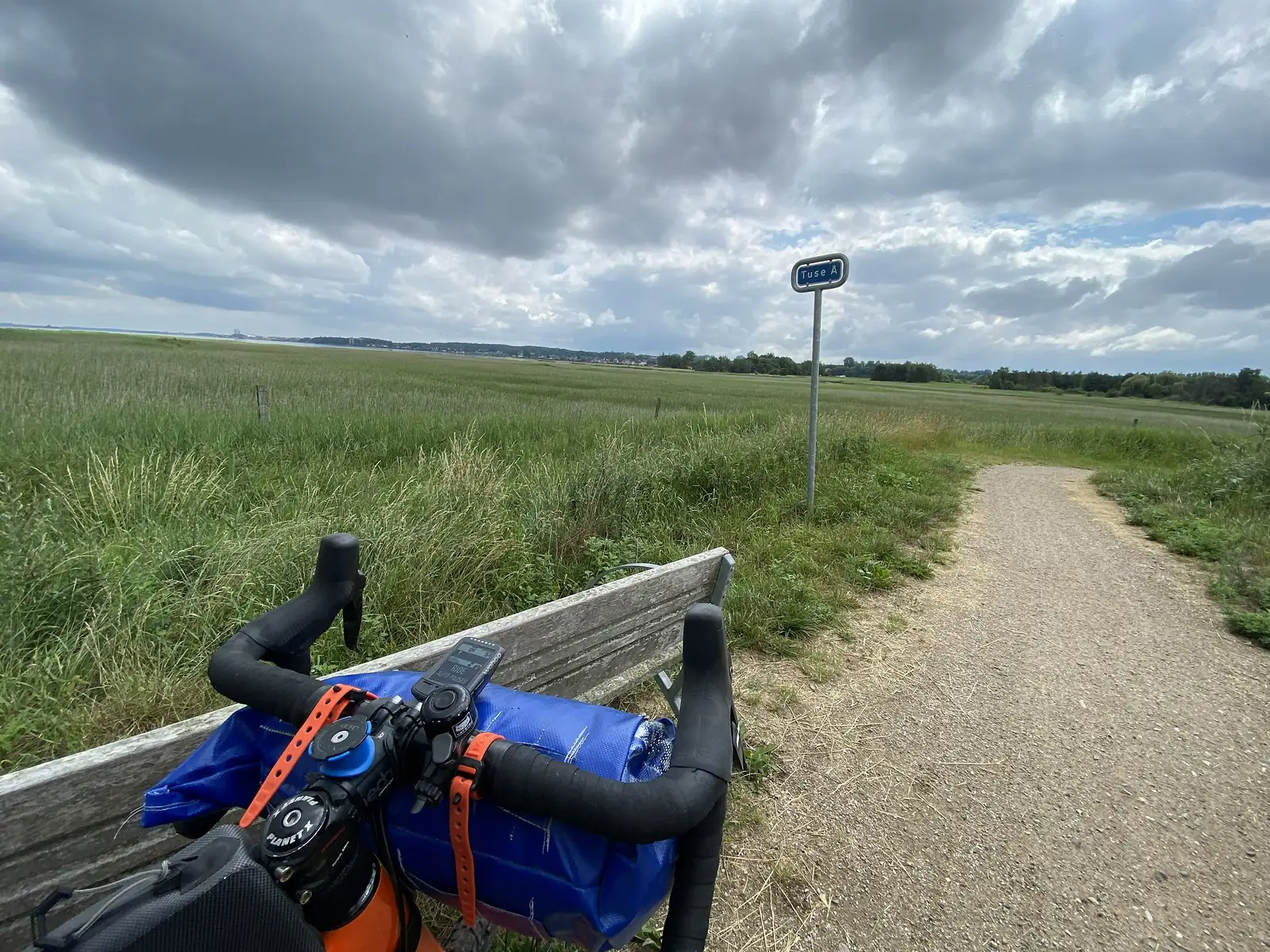 The handlebars of a bike with a homemade blue bar bag.