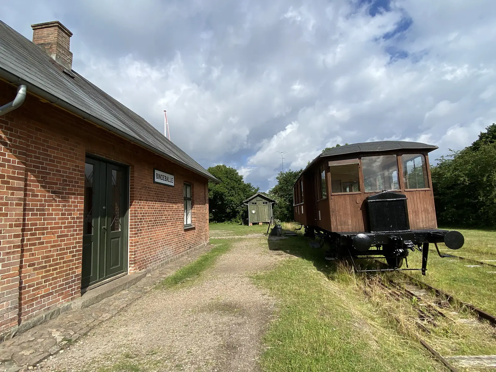 A red-brick railway station signed "BINDEBALLE", with an old wooden railcar standing on the grass-grown track beside it.