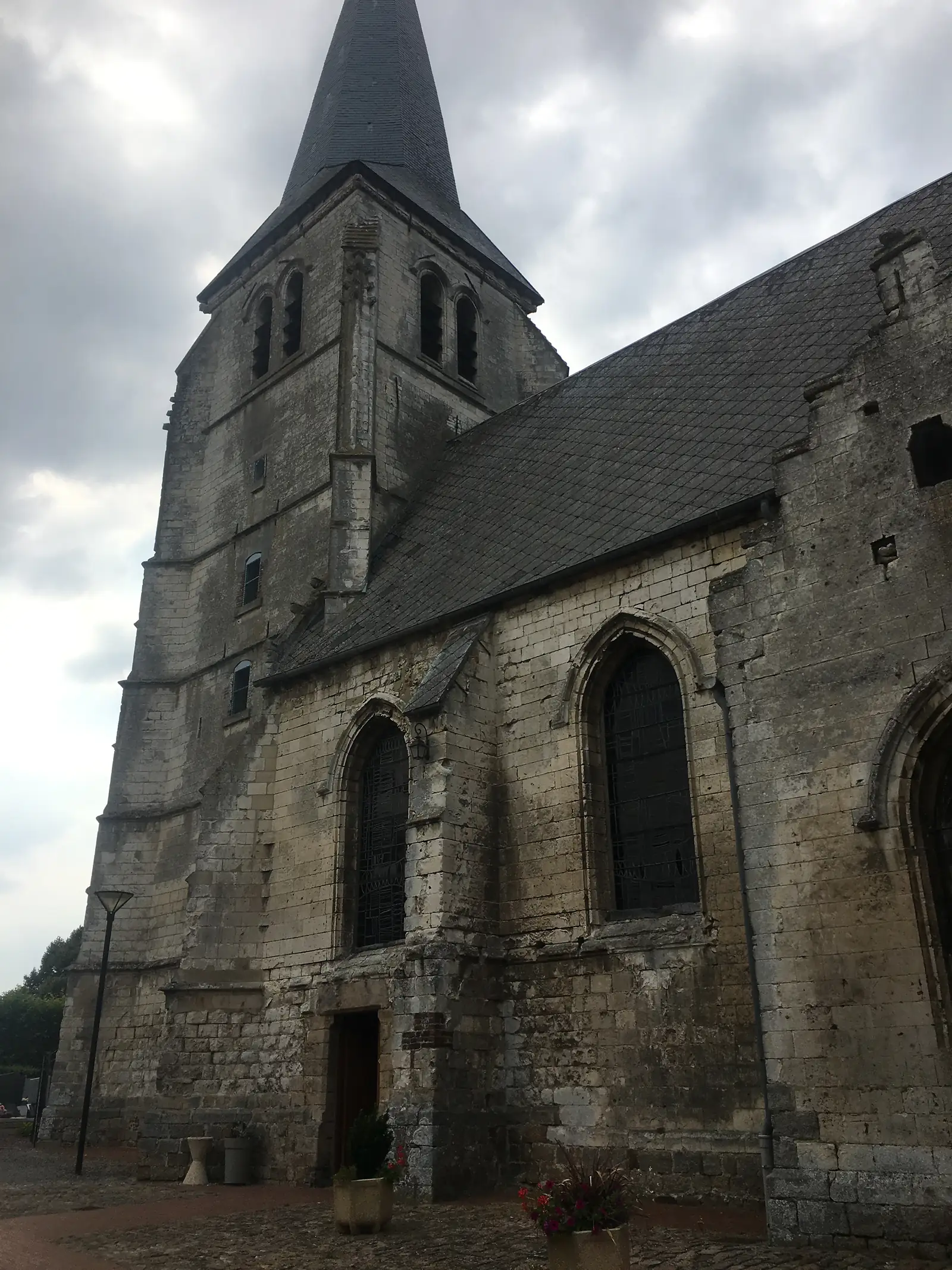 The weathered stone tower and slate-roofed nave of a village church rise against a cloudy sky.