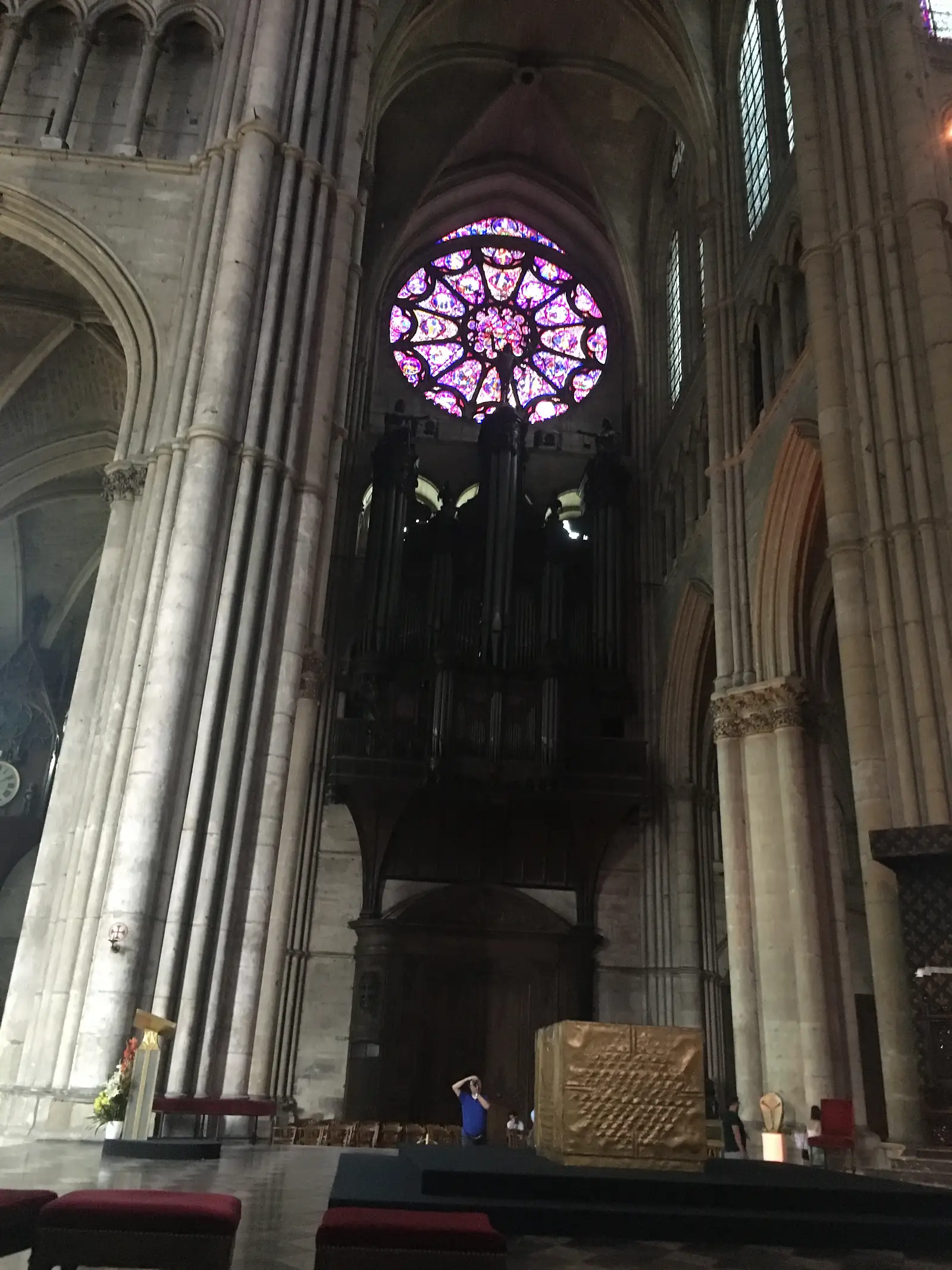 Visitors walking beneath the ribbed vaulting of Reims Cathedral's nave towards a distant rose window at the west end.