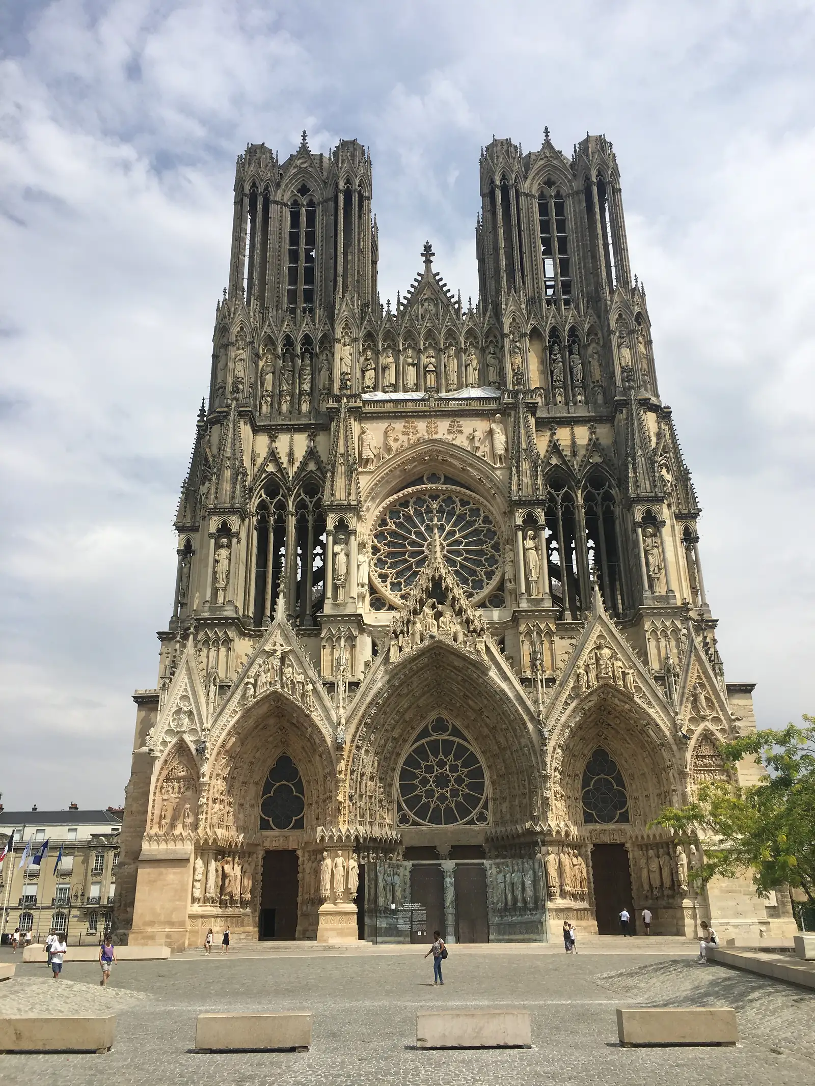 The twin gothic towers of Reims Cathedral seen from below, tracery and pinnacles silhouetted against a partly cloudy sky.