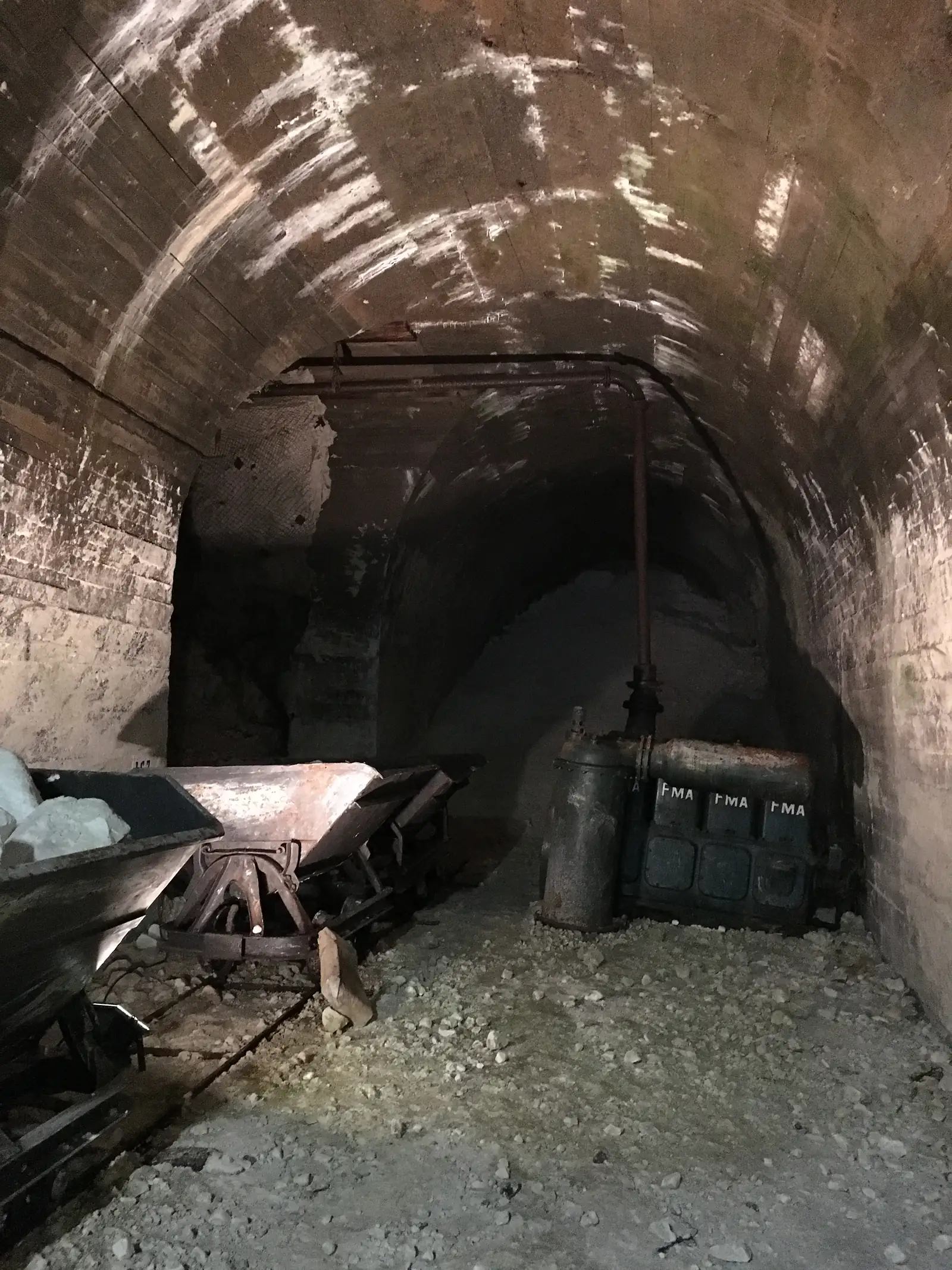 A large rusted cylindrical tank stencilled 'FMA', fed by looping pipework, stands in an alcove of the brick-lined tunnel.