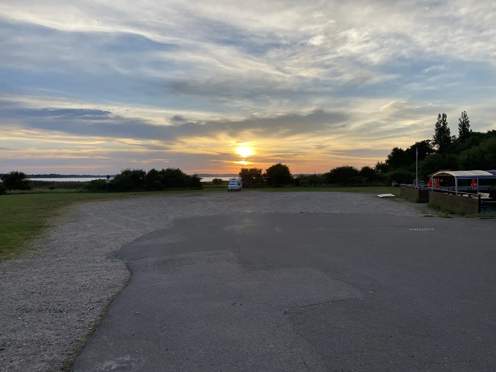 Sunrise over an empty gravel car park by the water, a single campervan parked near the shore.