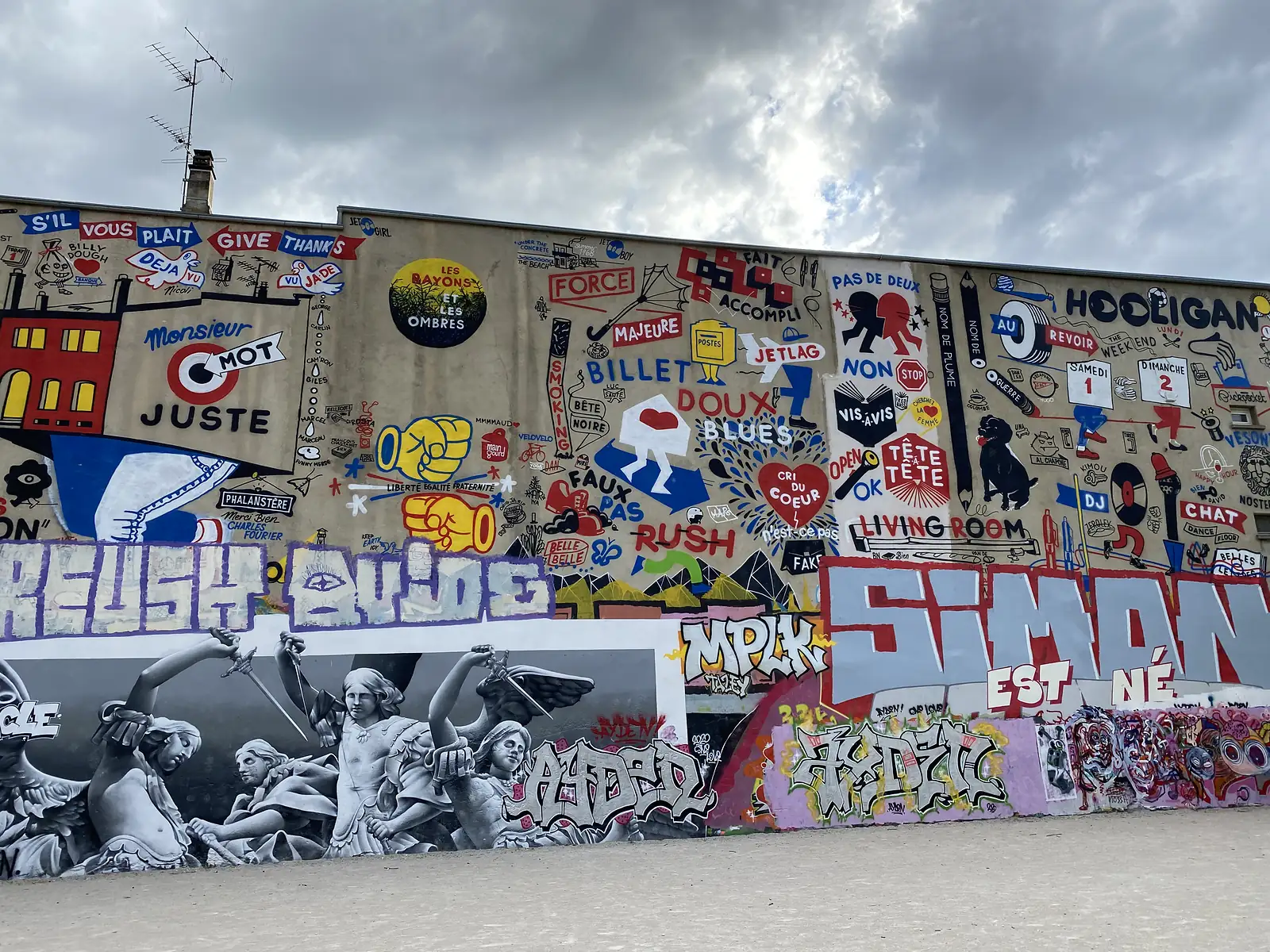A wall covered in street art features painted slogans such as 'Billet Doux', 'Faux Pas' and 'Hooligan' alongside a black-and-white mural of angel statues wielding daggers.