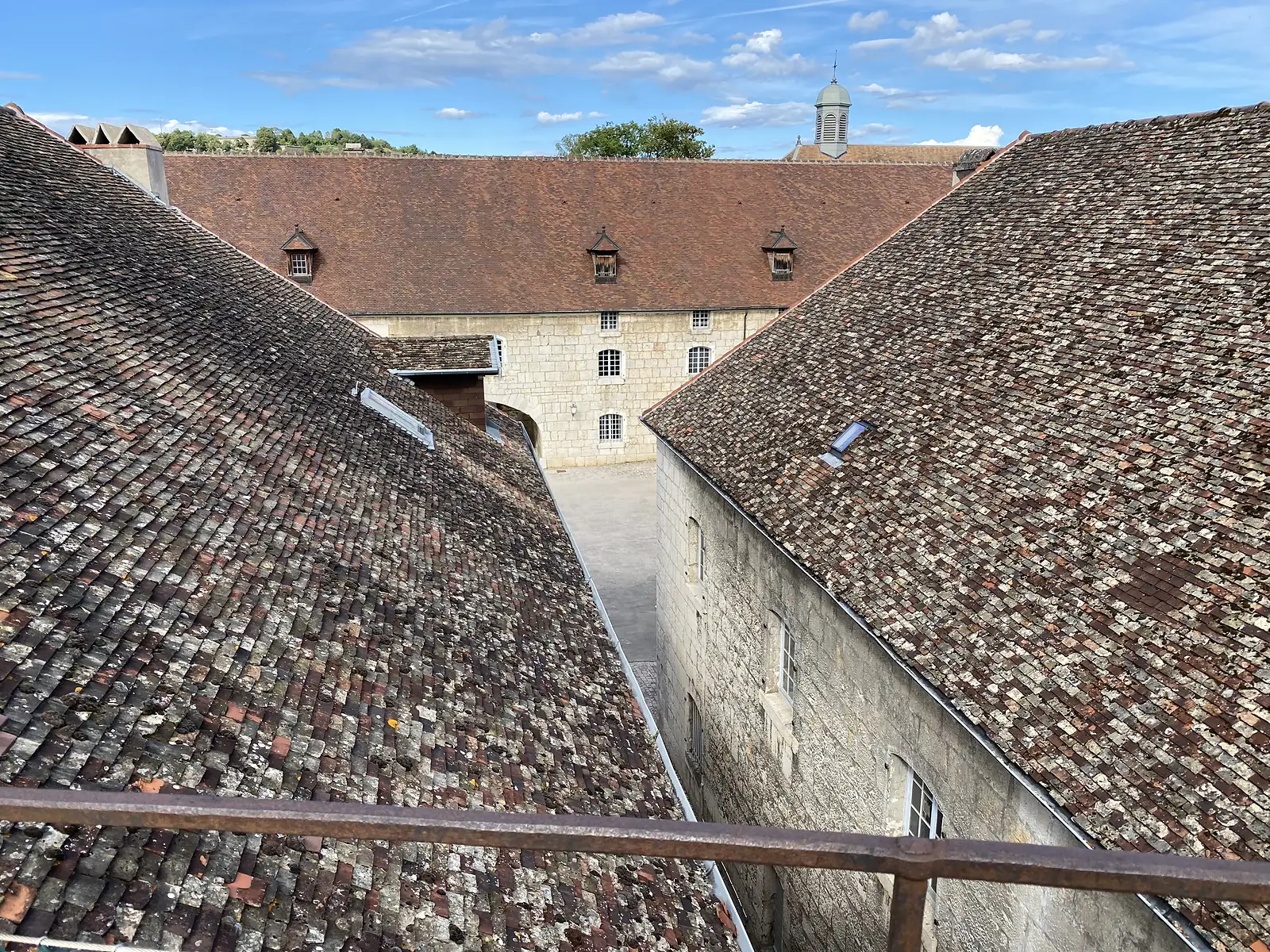 Terracotta-tiled rooftops of citadel buildings meet at a narrow gap above a stone courtyard, with a small cupola visible beyond.