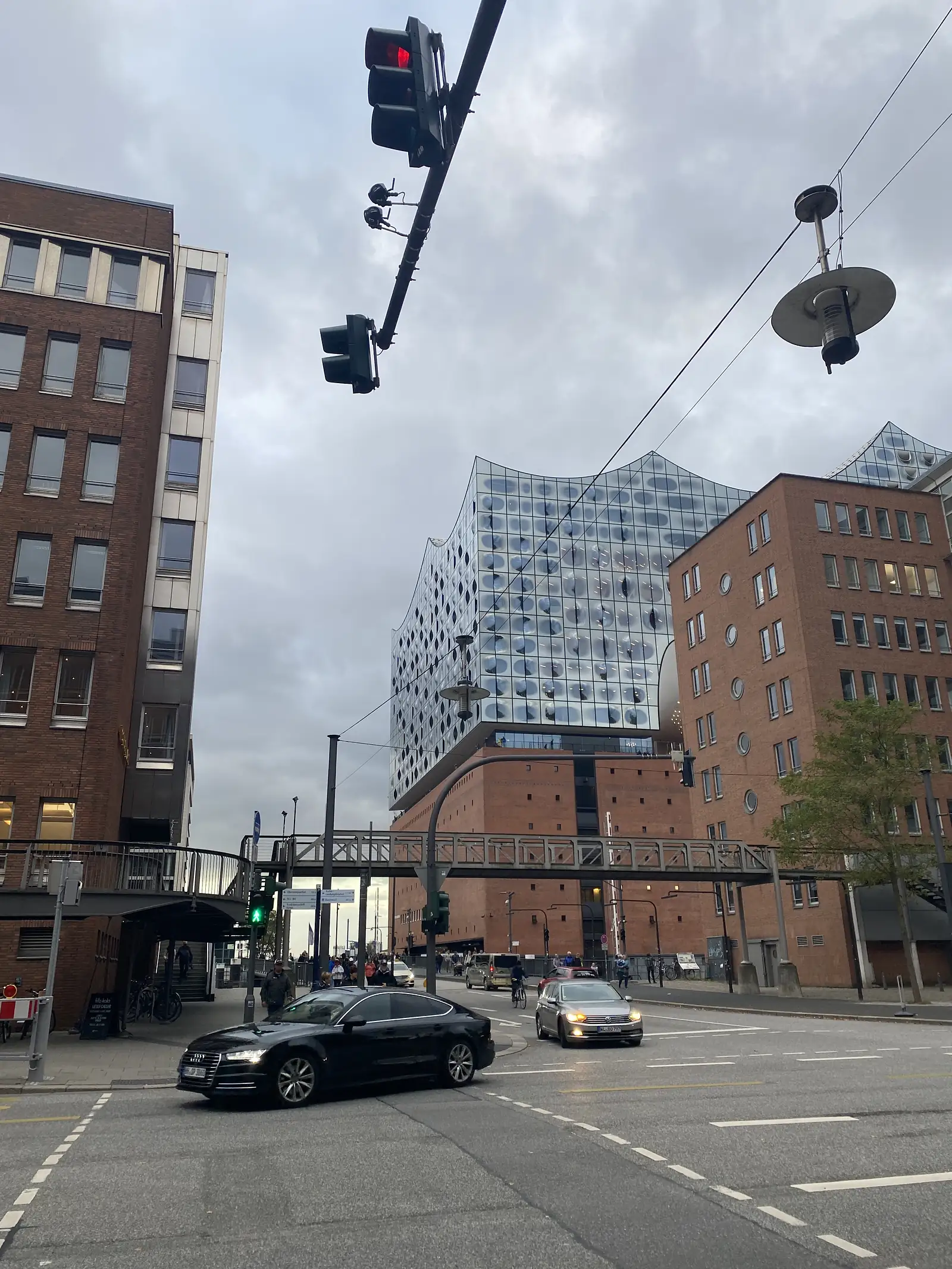 A modern building with a rippling glass facade rises above older brick warehouses at a city street junction with traffic waiting at the lights.