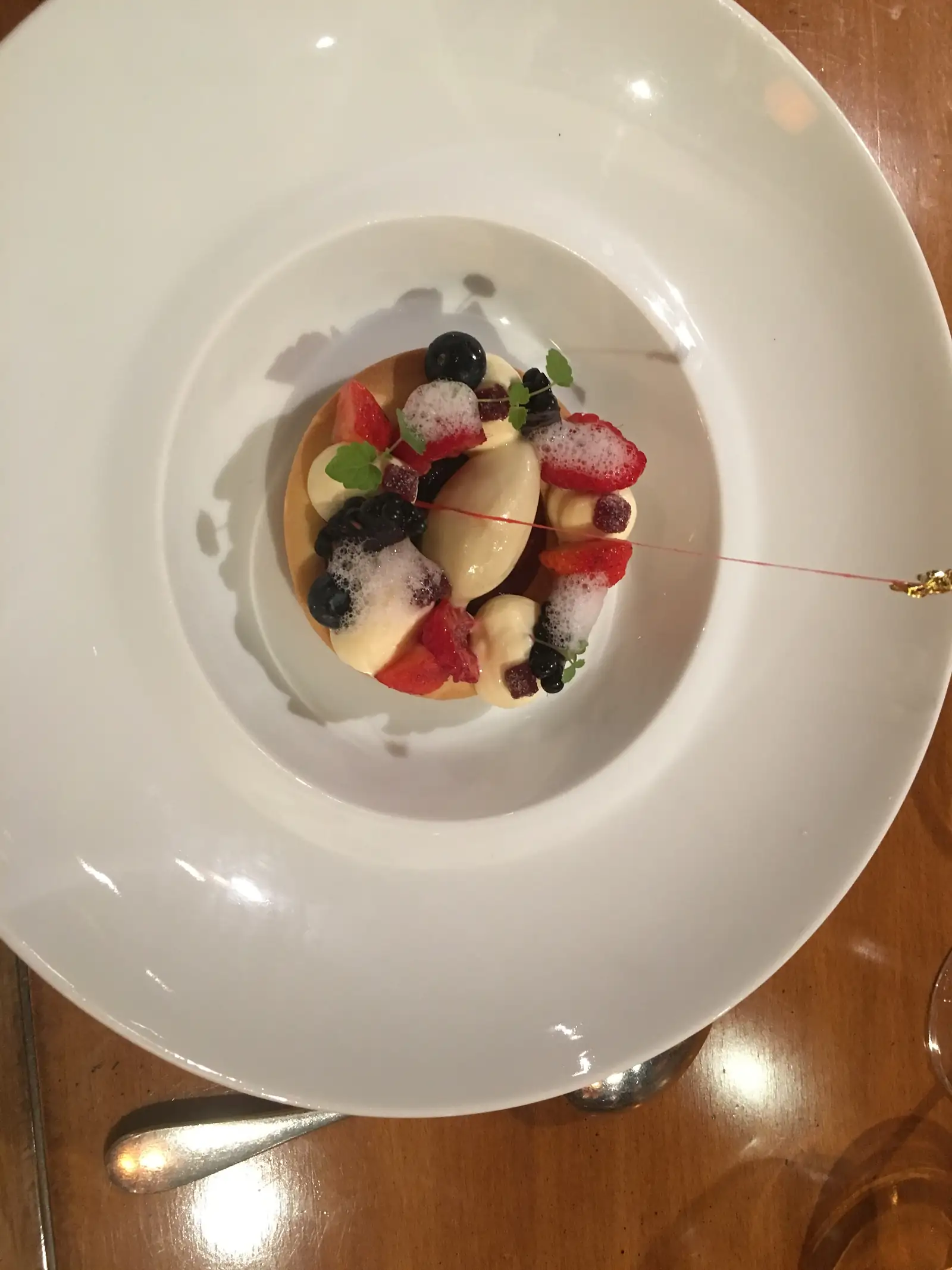A berry tart topped with strawberries, blackberries, blueberries and a quenelle of ice cream, with a thread of caramel being poured over it.