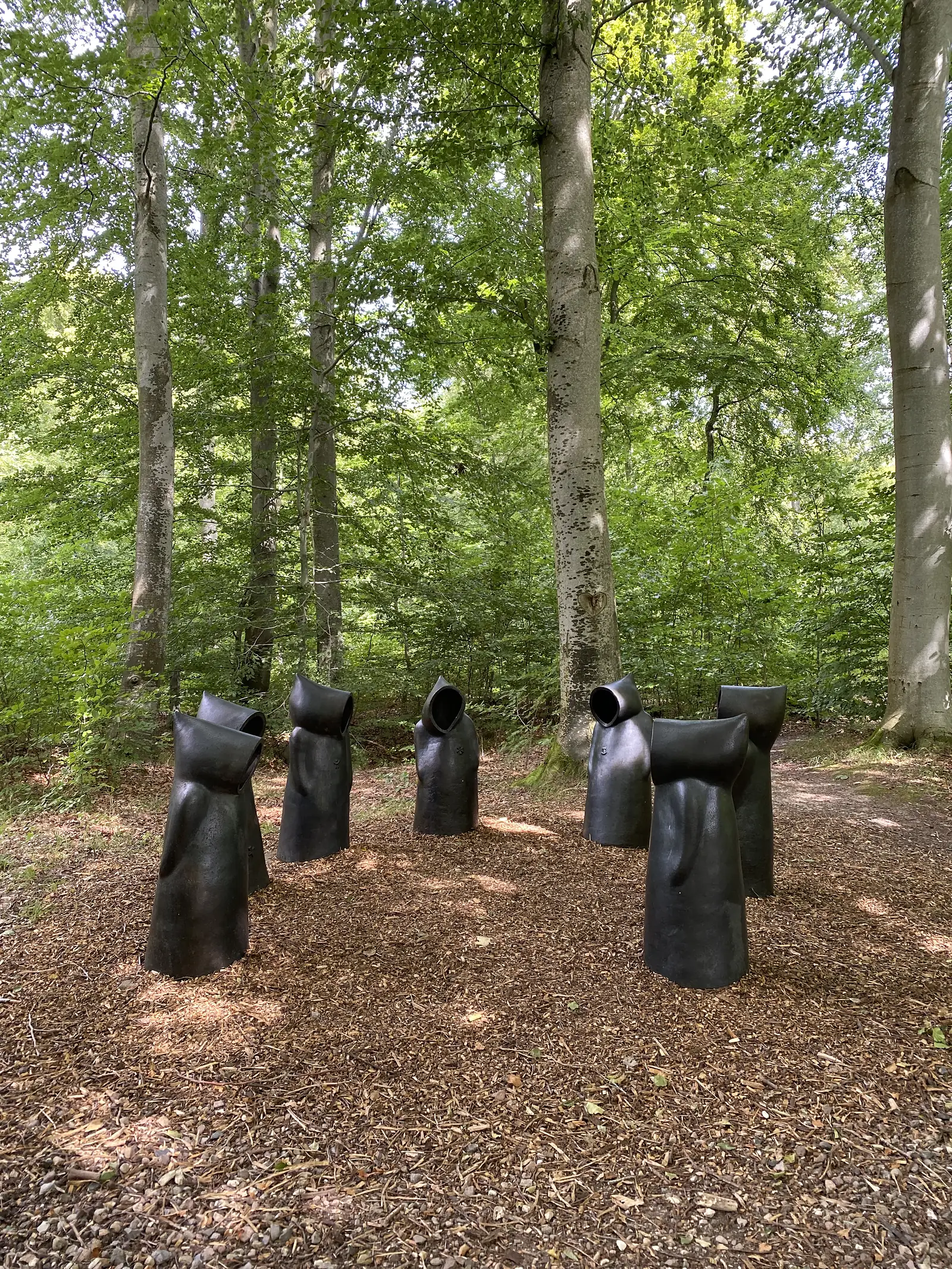 Sjælene, a group of dark hooded sculptures standing in the beech wood at Ulkerup.