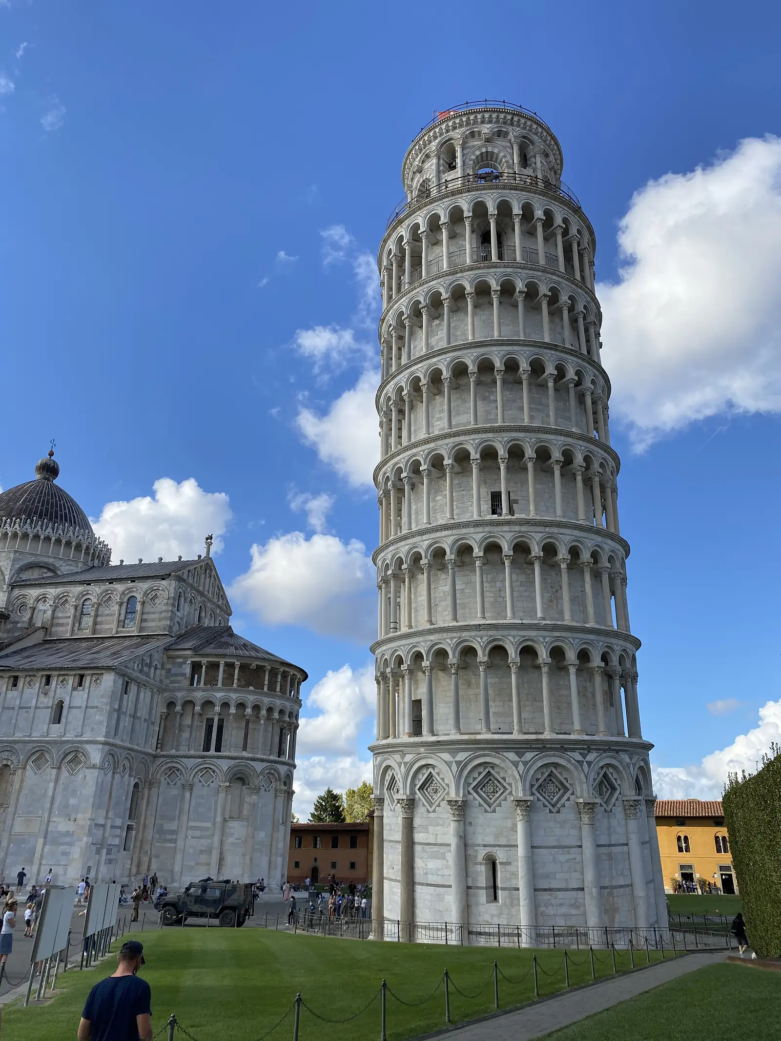 The Leaning Tower of Pisa's tiered marble arcades rise at an angle against a partly cloudy sky, with the cathedral's facade visible below.