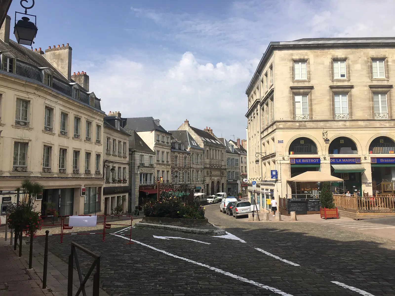 A cobbled street lined with pale stone townhouses opens onto a small square, with the sign for 'Le Bistrot de la Mairie' visible on a corner building.